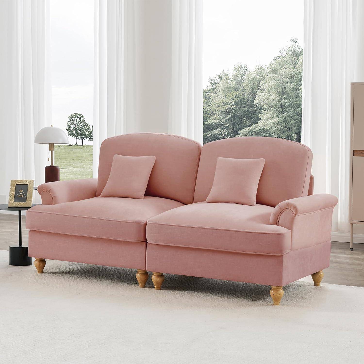 Rosa Zweisitzer-Sofa mit zwei passenden Kissen in einem hellen Wohnzimmer neben hohen Fenstern, mit einer Stehlampe und einem kleinen Tisch in der Nähe.