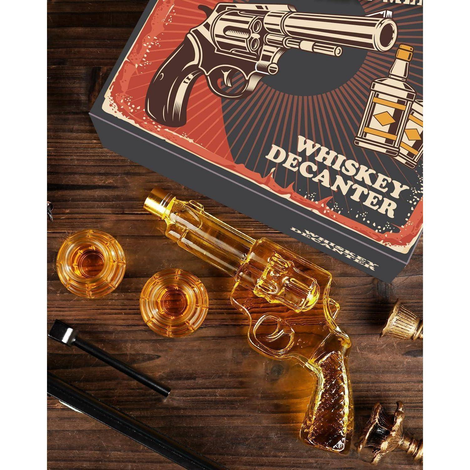 Geschenkbox mit der Bezeichnung „Whiskey Karaffe" mit einer revolverförmigen Glaskakraffe, zwei Gläsern und Zubehör auf einem Holztisch.