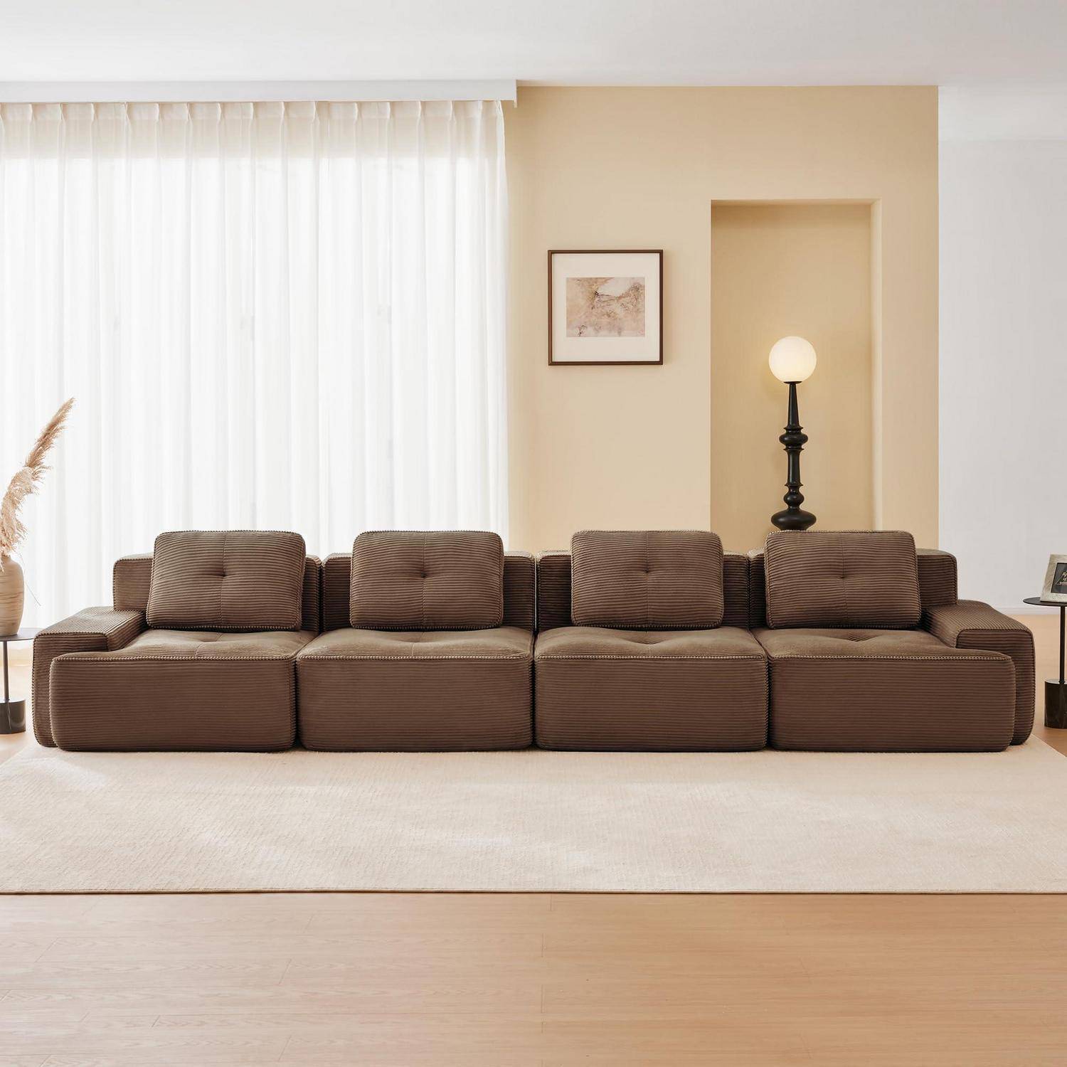 Modernes Wohnzimmer mit langem braunem Modulsofa, beigem Teppich, transparenten Vorhängen, gerahmten Kunstwerken und einer beleuchteten Stehlampe in einer vertieften Wandnische.