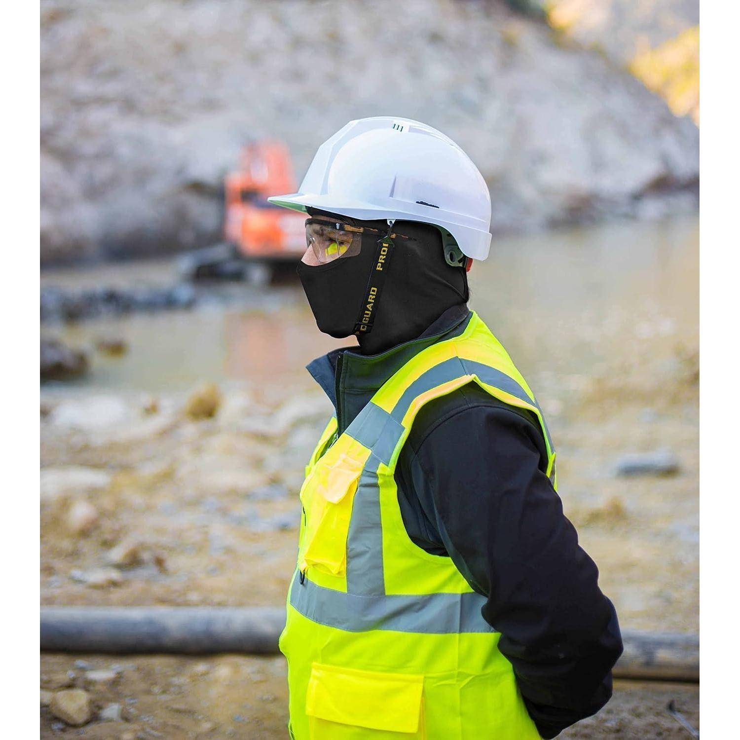 Bauarbeiter in weißem Schutzhelm, Schutzbrille, Gesichtsschutz und Warnweste, der auf einer felsigen Baustelle steht.