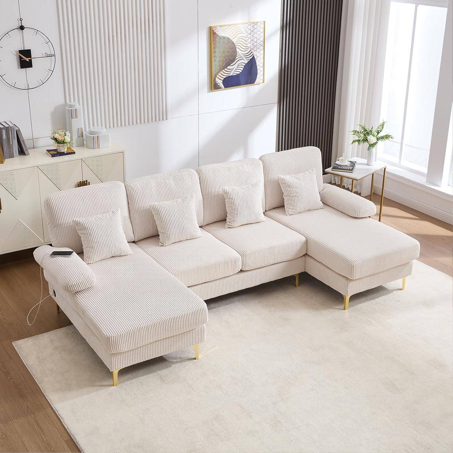 Cremefarbenes Cord-Ecksofa mit Chaiselongue, passenden Kissen und goldfarbenen Beinen in einem hellen, modernen Wohnzimmer.