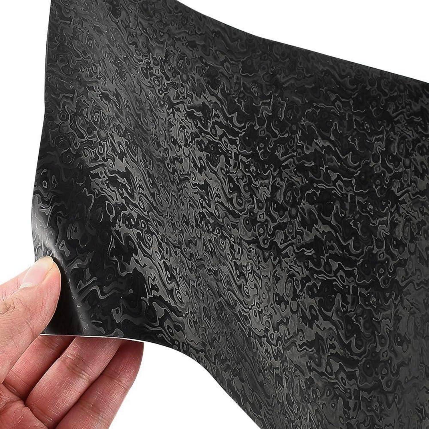 Eine Hand, die ein flexibles schwarzes marmoriertes Blatt mit einer welligen, glänzenden Oberfläche gegen einen weißen Hintergrund hält.