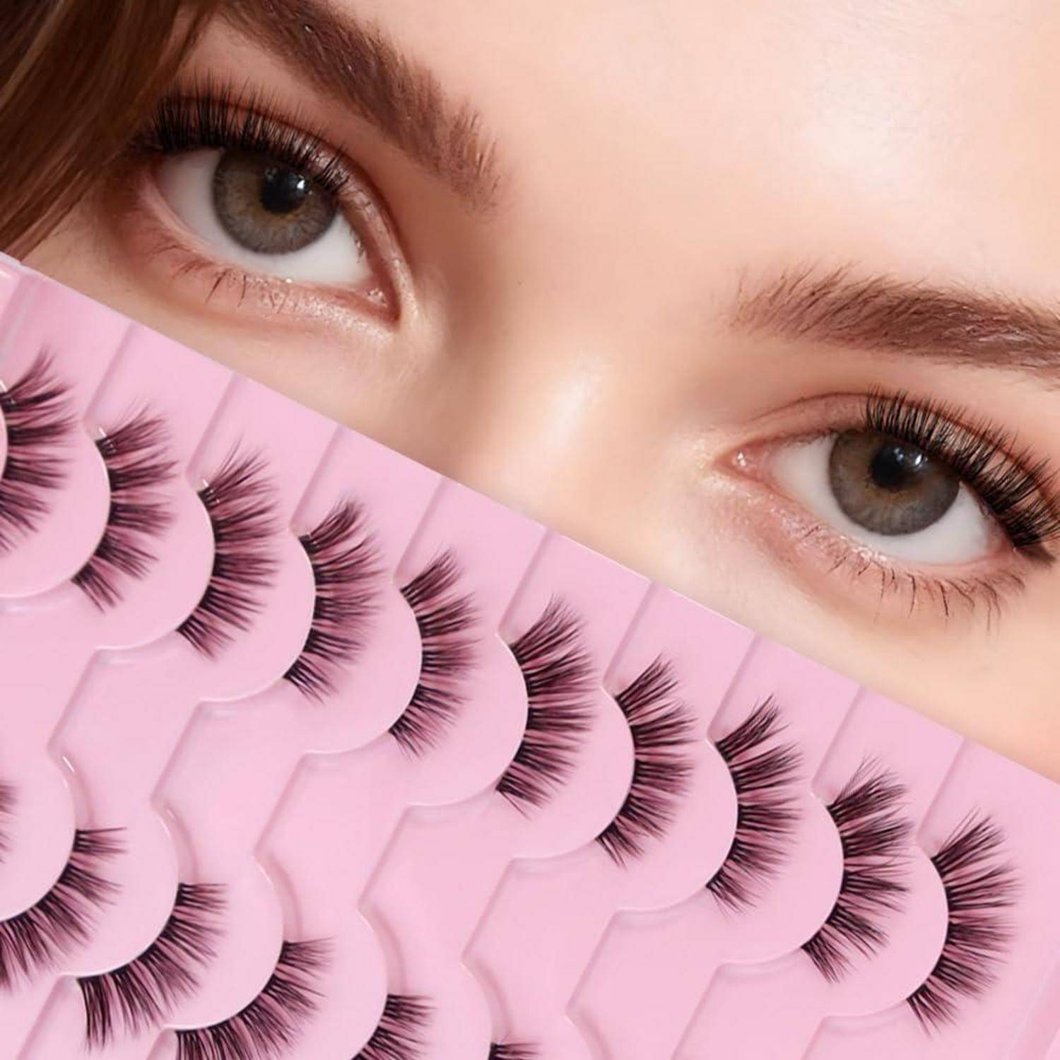 Nahaufnahme von Augen mit langen Wimpern hinter einem Fächer von künstlichen Wimpern, die auf rosa Verpackung präsentiert werden.