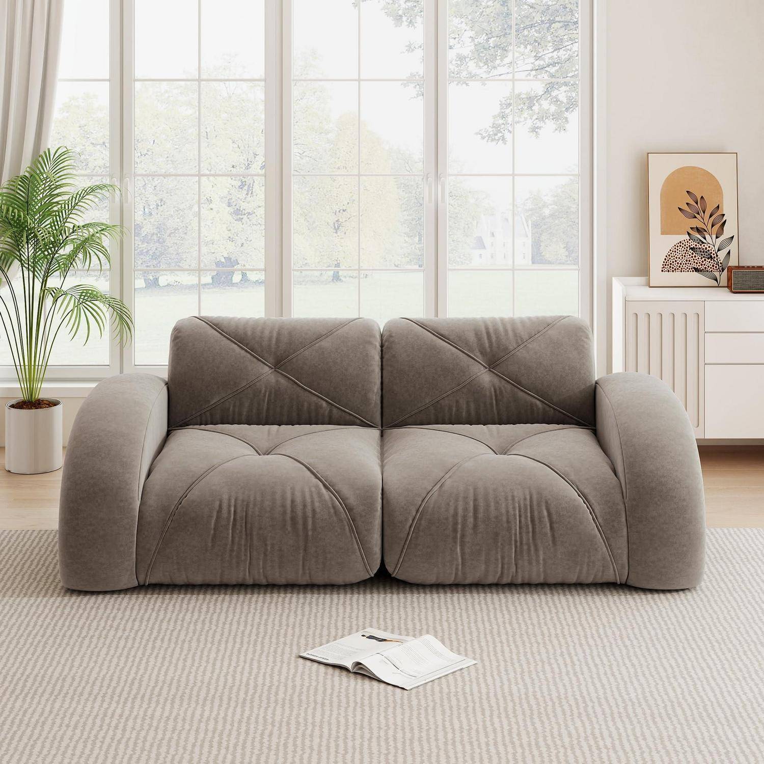 Weiches graues Zweisitzer-Sofa in einem hellen Wohnzimmer mit einer Pflanze, einem Sideboard und einem offenen Magazin auf dem Boden.