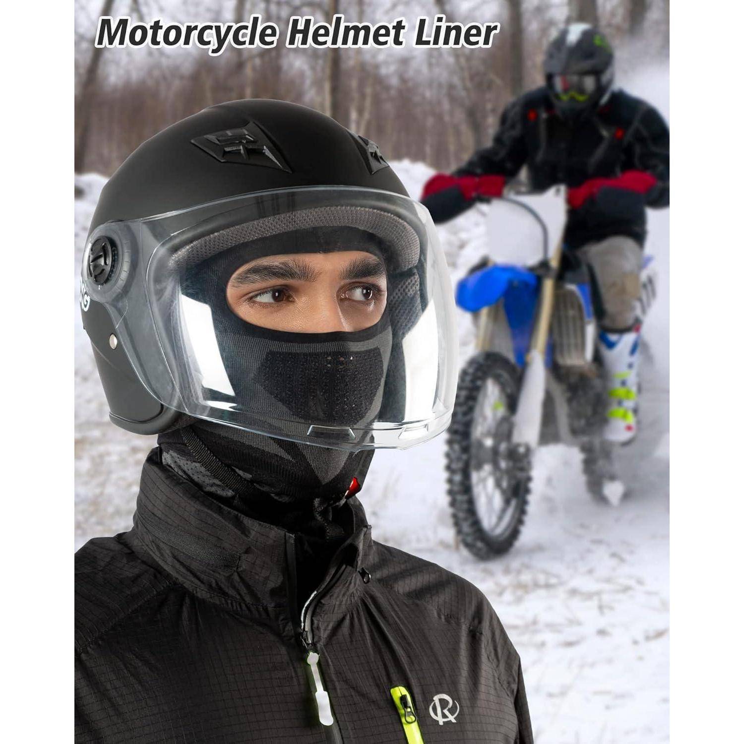 Person trägt einen schwarzen Motorradhelm mit klarem Gesichtsschutz und Innenfutter, mit einem weiteren Fahrer auf einem Dirt Bike im verschneiten Hintergrund.