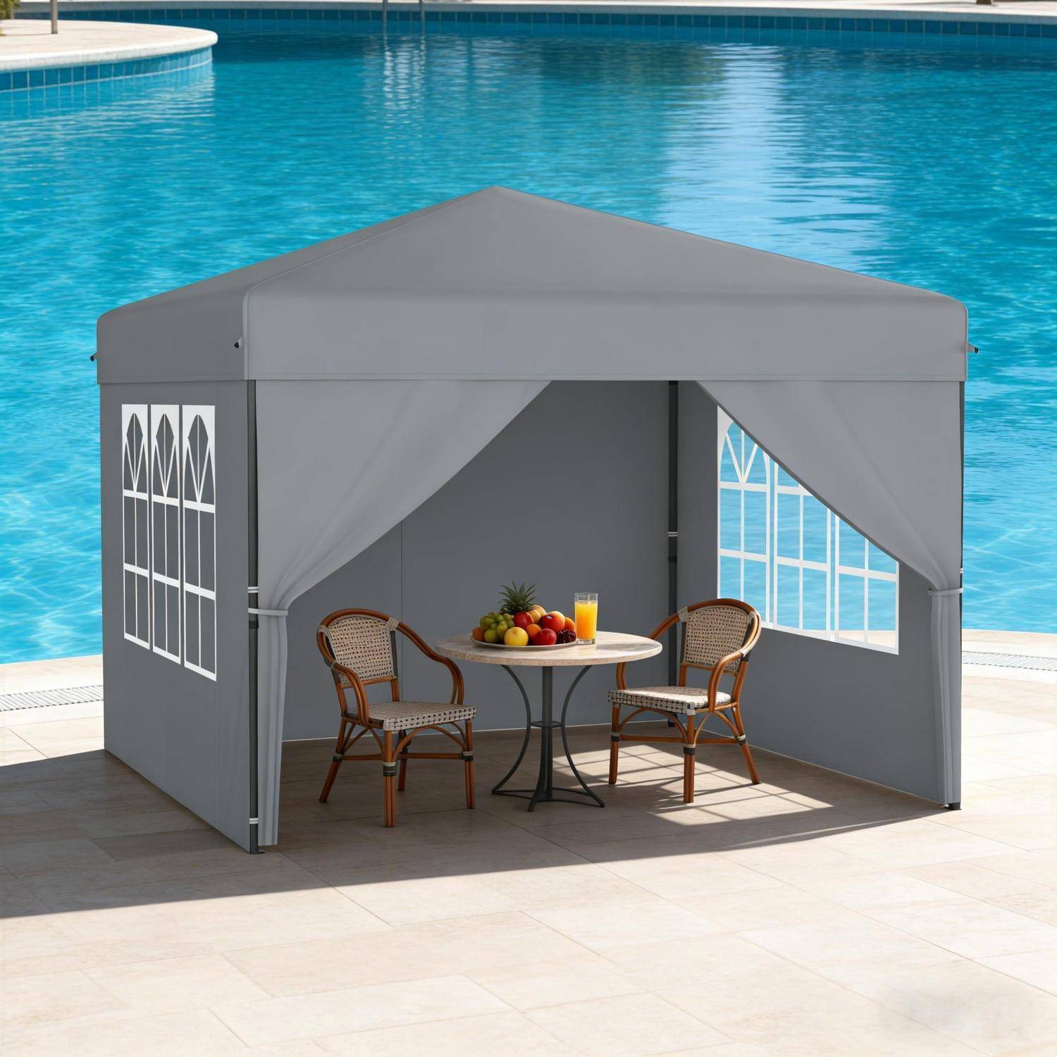 Grauer Patio-Pavillon neben einem Pool mit zwei Rattanstühlen und einem kleinen runden Tisch, auf dem Obst und Getränke stehen.
