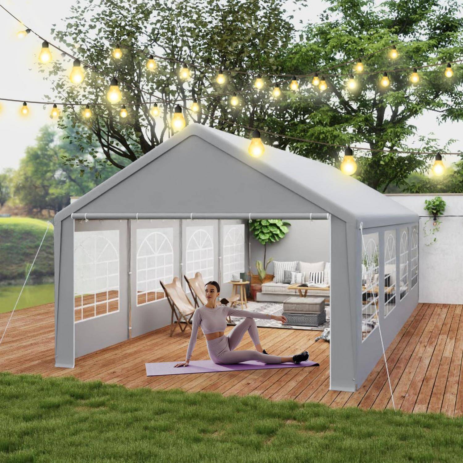 Eine Frau, die auf einer Matte Yoga macht, in einem grauen Außenzelt auf einer Holzterrasse, mit Lounge-Möbeln und Lichterketten über ihr.