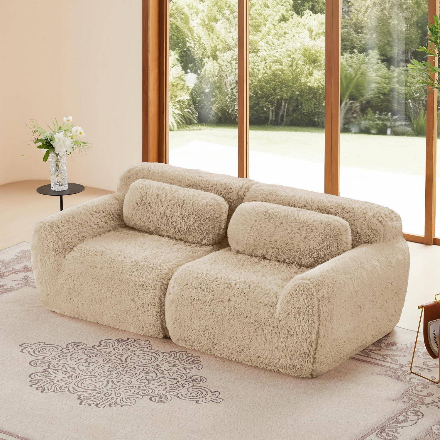Beiges flauschiges Sofa in einem hellen Raum mit großen Fenstern und einem Blumenteppich; ein kleiner Beistelltisch mit Blumen steht in der Nähe.