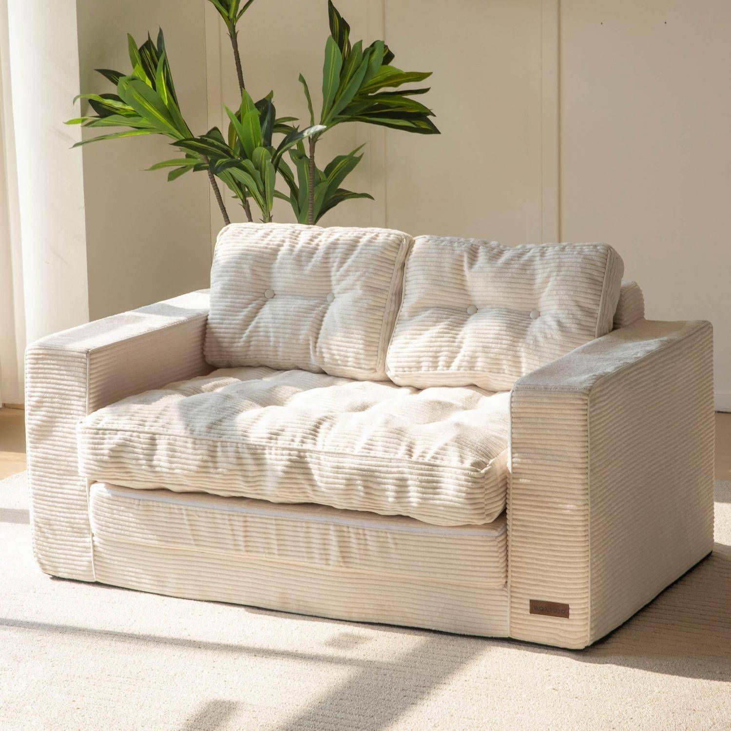 Cremefarbenes gestreiftes Zweisitzer-Sofa mit gesteppten Kissen in einem hellen minimalistischen Raum, dahinter eine hohe grüne Pflanze.