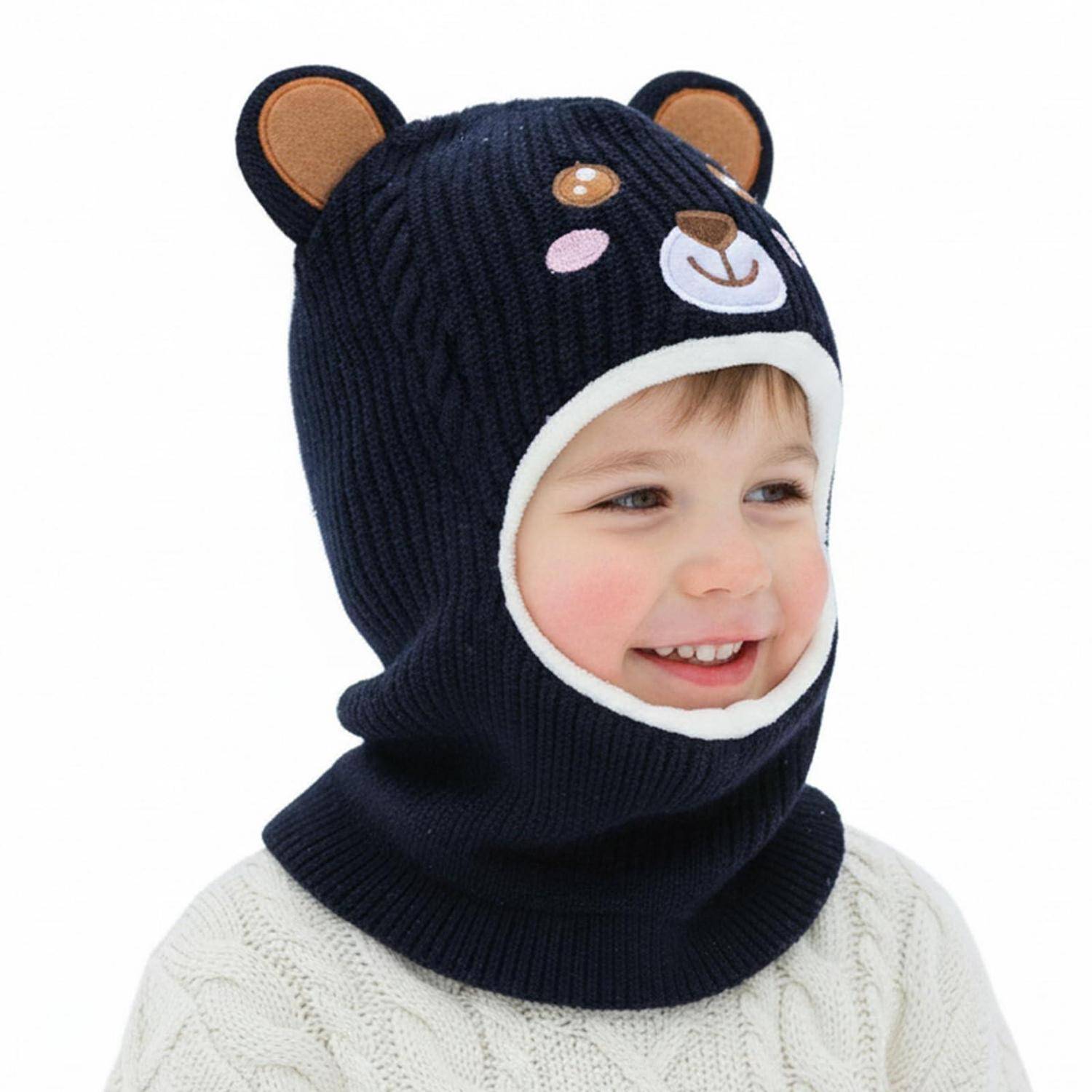 Lächelndes Kind, das eine dunkelblaue gestrickte Bärenmütze mit Ohren und Gesichtsöffnung trägt, vor weißem Hintergrund gezeigt.