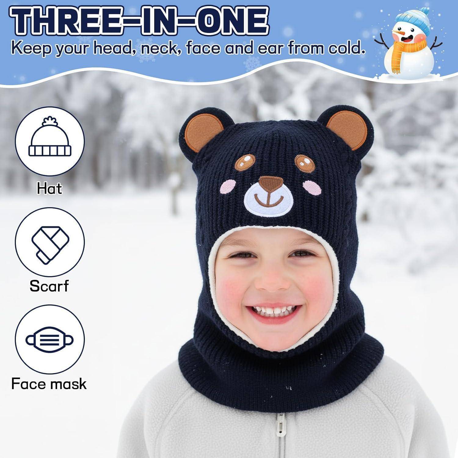 Kind trägt eine dunkelblauе Wintermütze mit Bären-Design, die drei Funktionen in einem erfüllt und Kopf, Hals und Gesicht bedeckt; Etiketten zeigen Mütze, Schal und Gesichtsmaske.