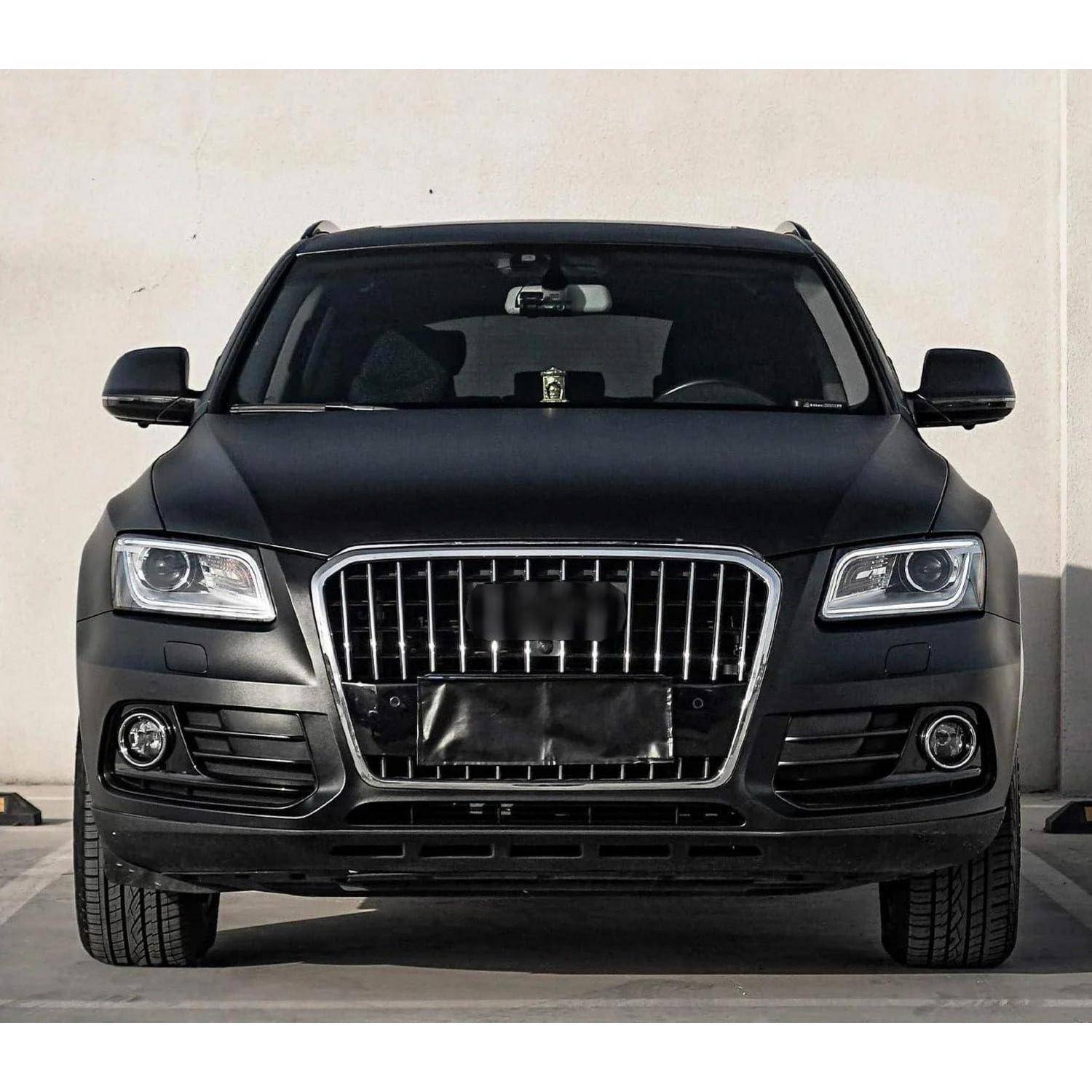 Frontansicht eines matten schwarzen SUV mit einem großen Chromgrill, geparkt vor einer schlichten Wand.
