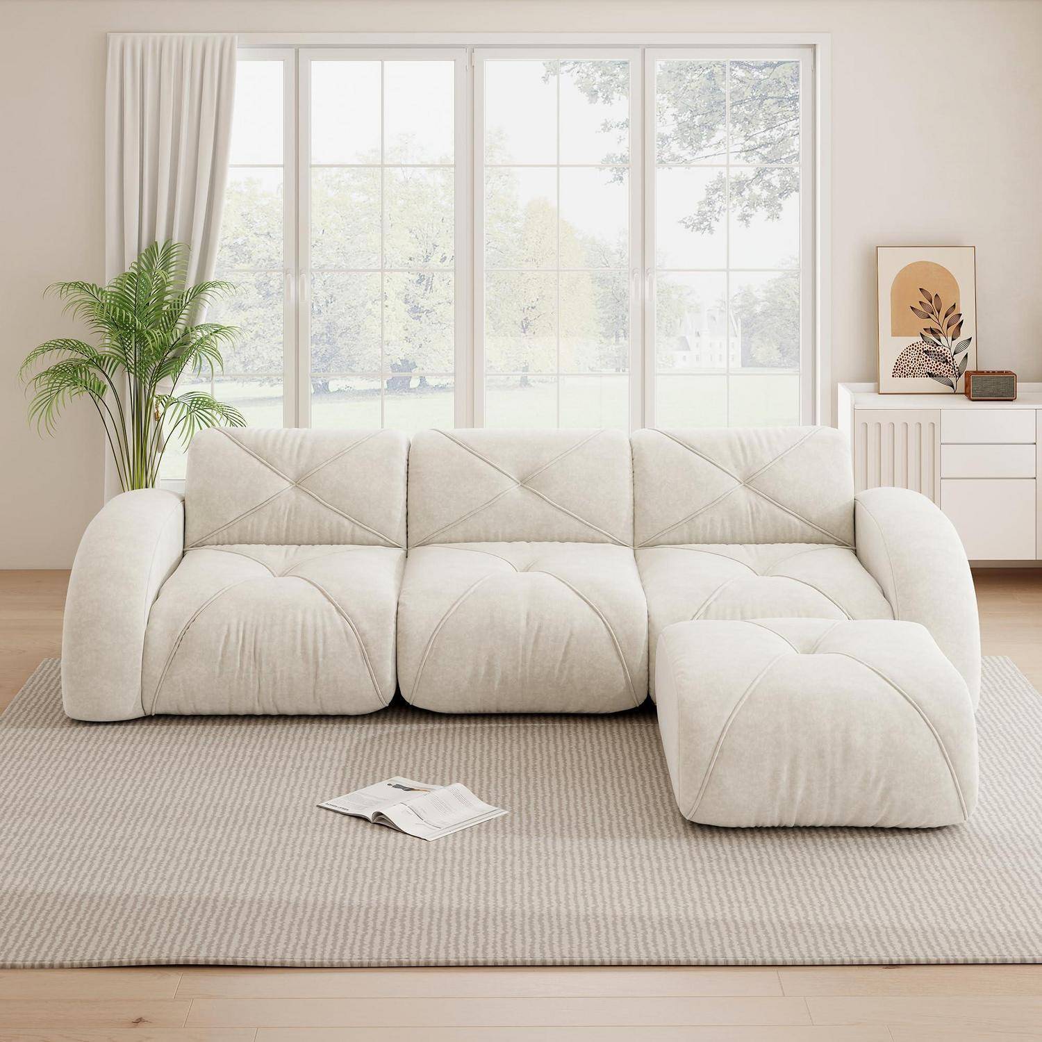 Cremefarbenes modulares Sofa mit Chaiselongue in einem hellen minimalistischen Wohnzimmer, vor großen Fenstern und neben einer Pflanze und einem Seitenschrank.