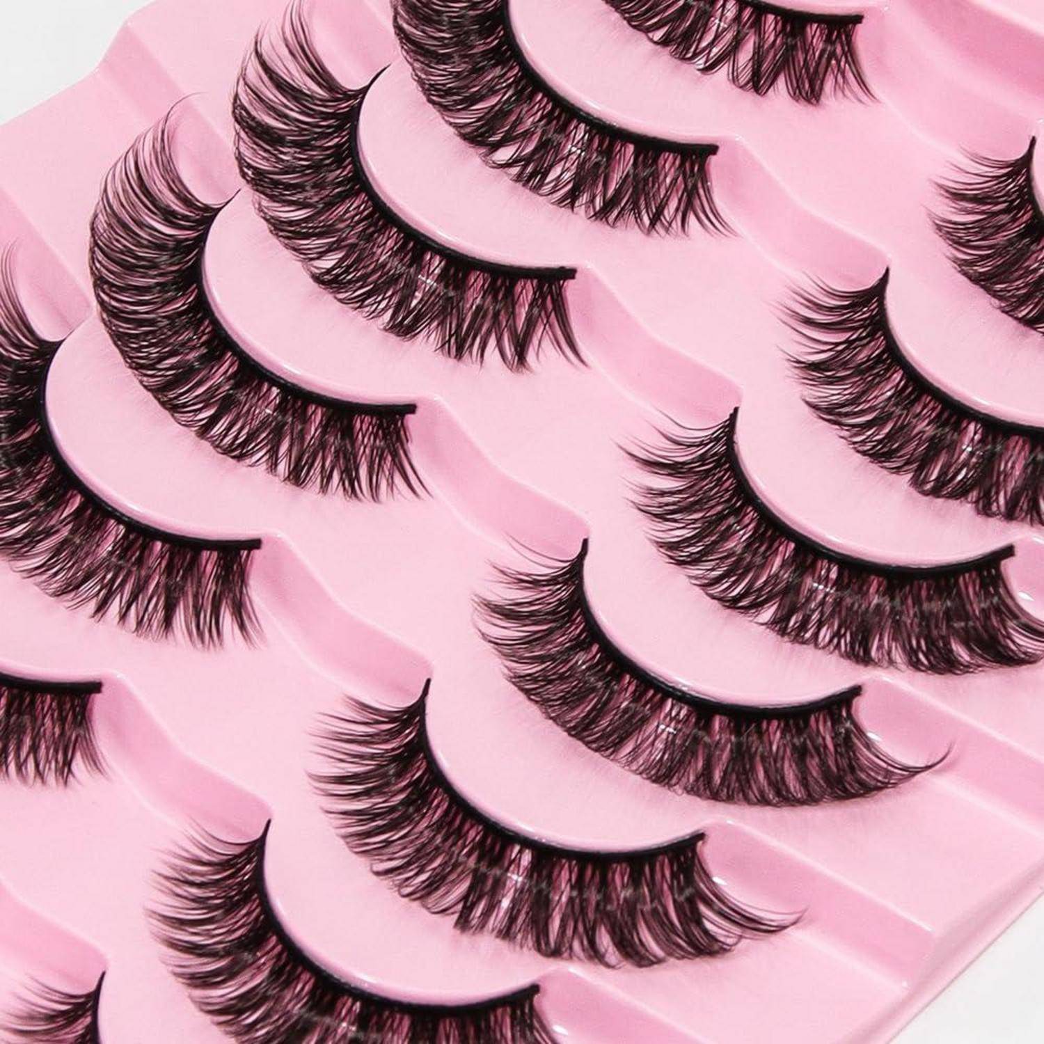 Mehrere Paare künstlicher Wimpern auf einem rosa Tablett ausgestellt, in Reihen angeordnet.