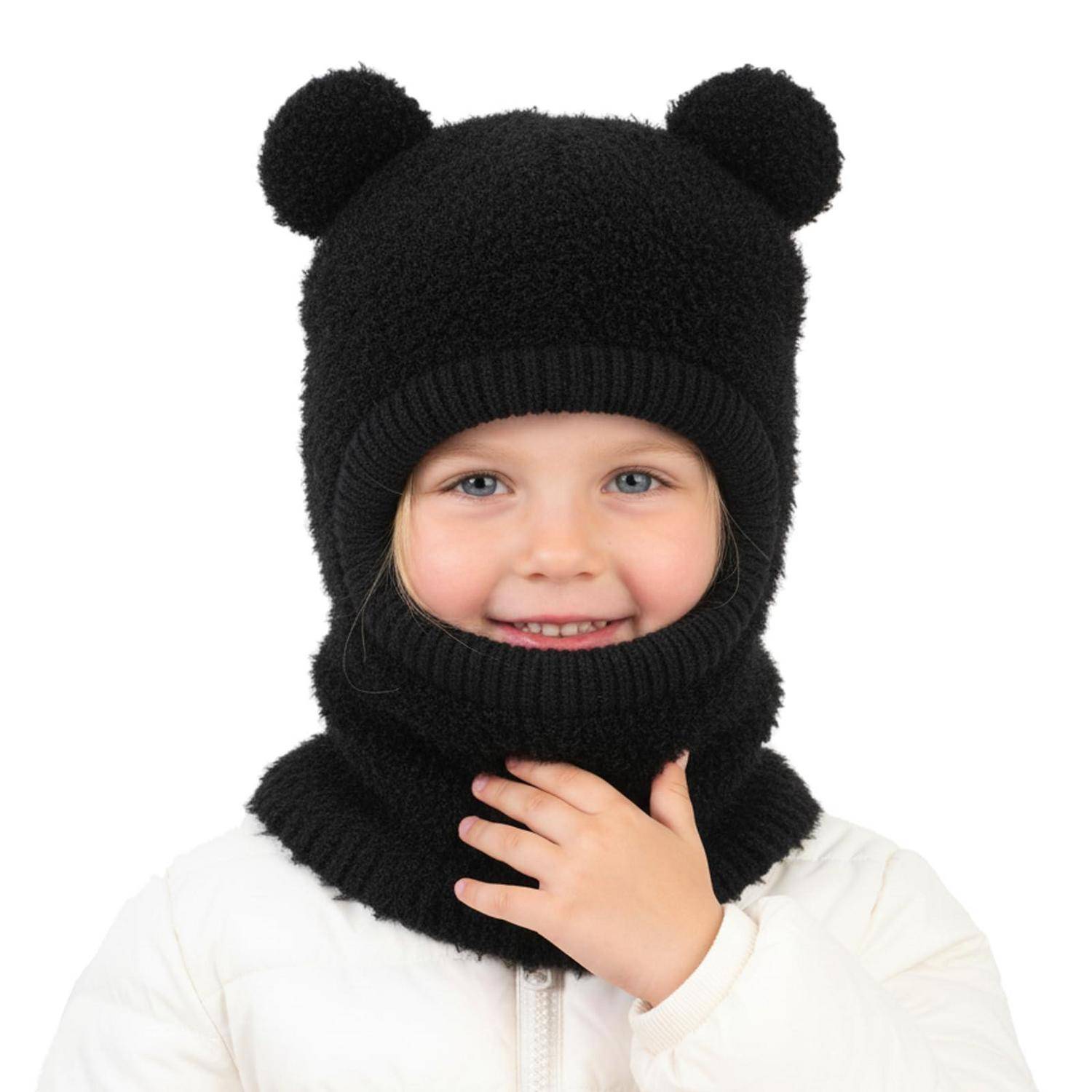Kind mit Lächeln, das eine schwarze gestrickte Bärenmütze mit Öffnungen für die Ohren und eine passende Gesichtsbedeckung trägt, vor weißem Hintergrund.