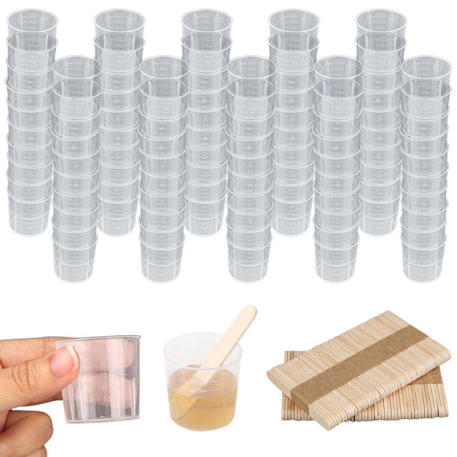 Satz aus durchsichtigen, wegwerfbaren Plastikbechern in Stapeln, mit einem Becher in der Hand gehalten, einem mit Flüssigkeit gefüllten Becher mit Rührstab und einem Stapel aus Holzrührern.