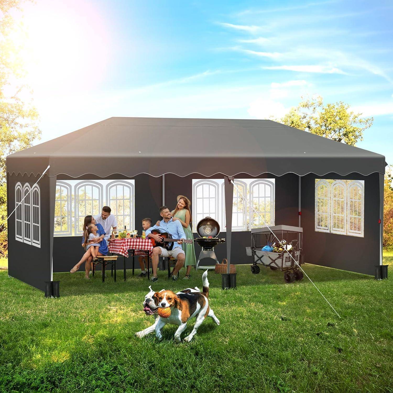 Eine Familie genießt ein Treffen im Hinterhof unter einem großen schwarzen Baldachindach, mit einem Grillgerät, einem Tisch und einem Hund, der im Gras herumläuft.