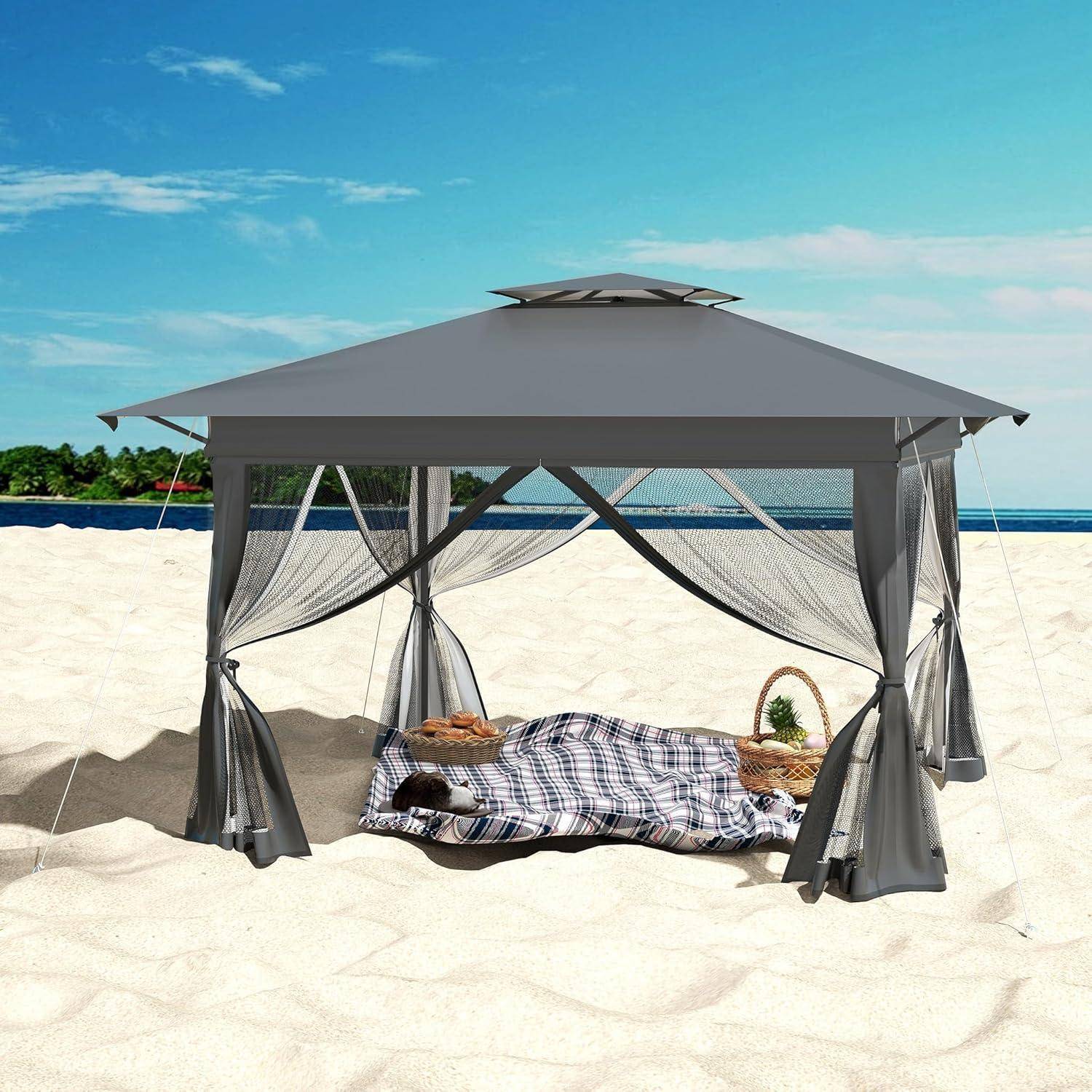 Überdachtes Zelt auf einem sandigen Strand mit einem Bett darunter, Vorhängen an den Seiten und einem Picknickkorb, mit Blick auf den Ozean.