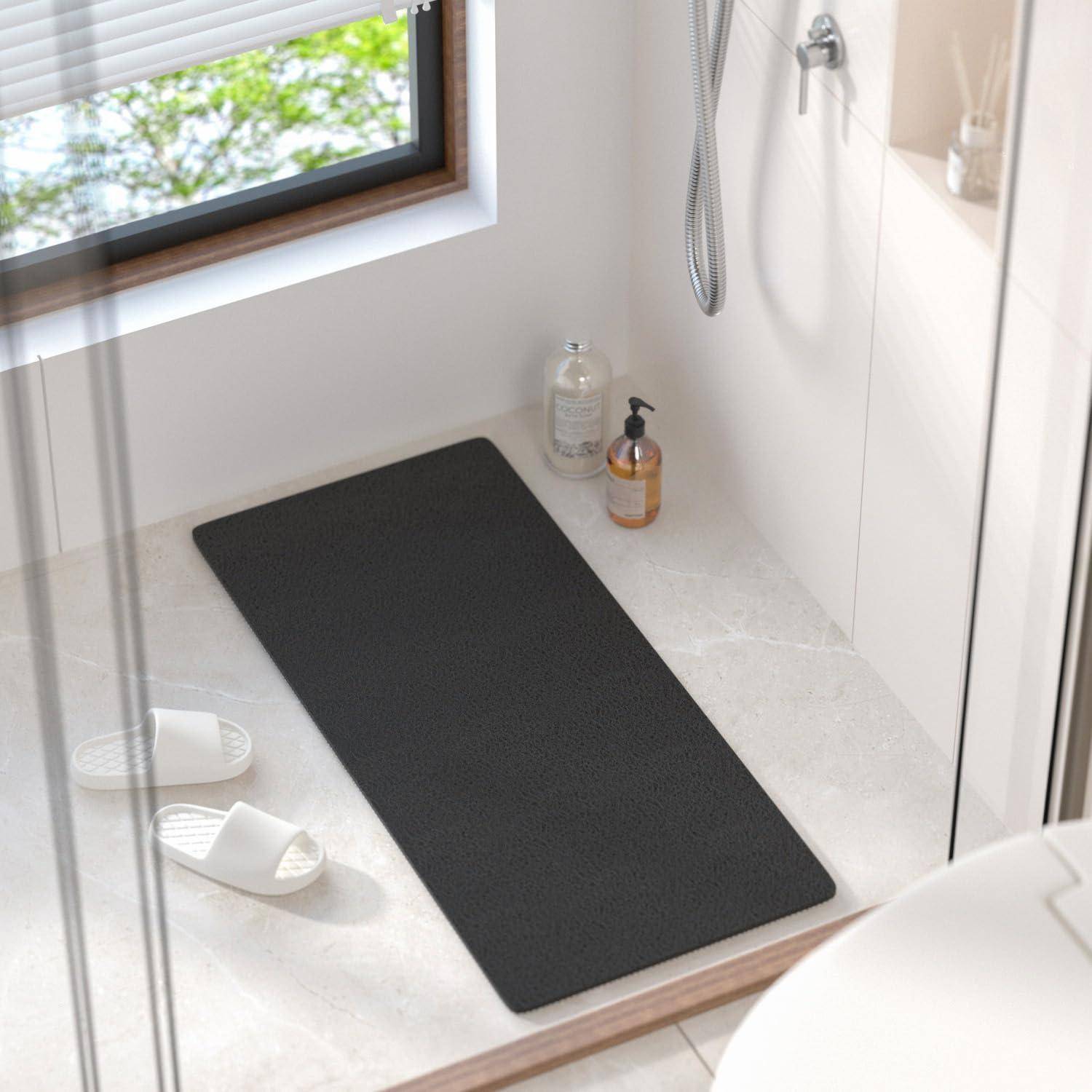 Minimalistisches Badezimmer mit schwarzer Bodenmatte, weißen Pantoffeln und Dusch-Toilettenartikeln neben einem fensterbeleuchteten Duschbereich.