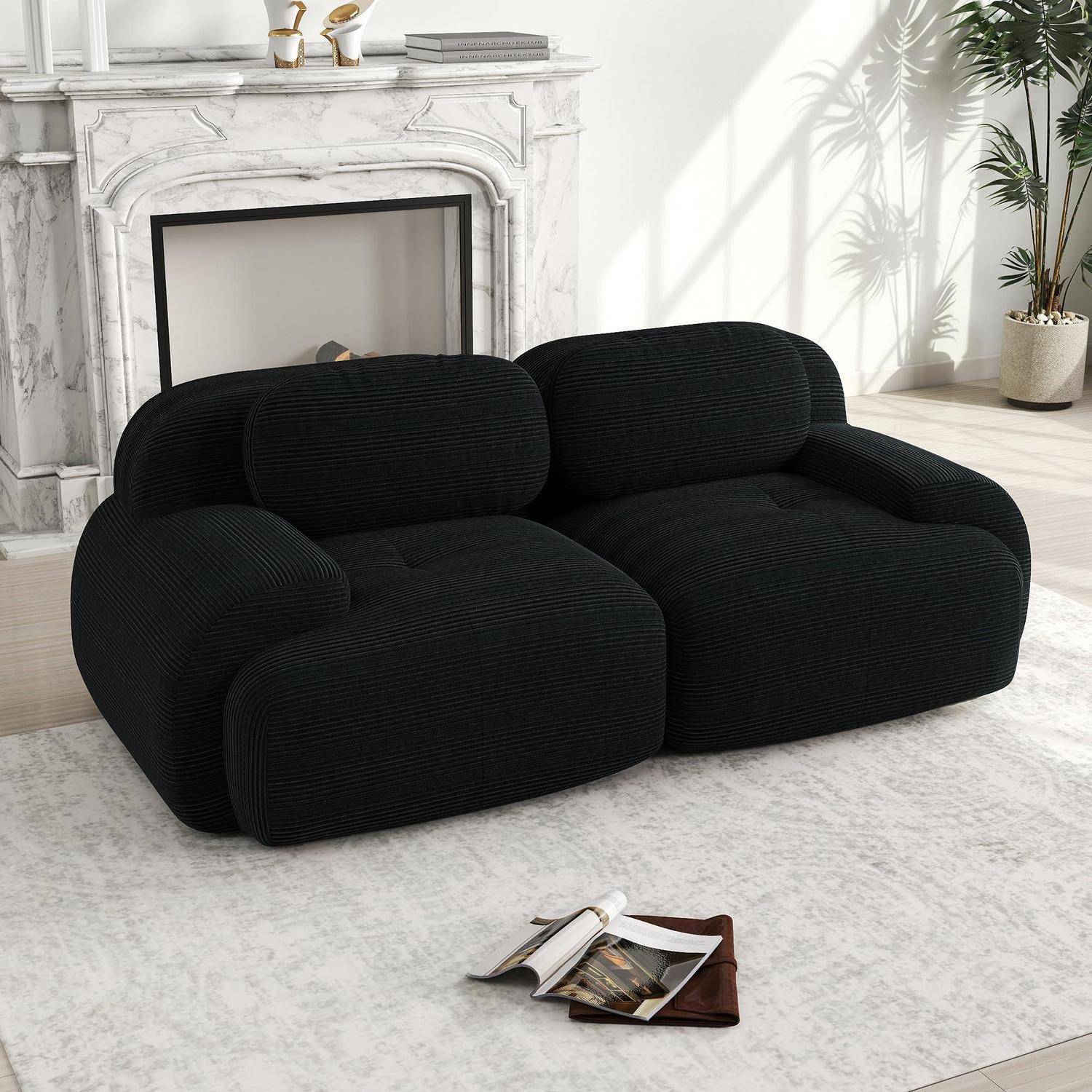 Schwarzes plüschiges Zweisitzer-Sofa in einem hellen Wohnzimmer mit weißem Kamin, Teppich und Pflanze.
