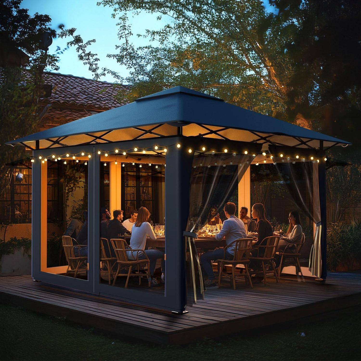 Menschen, die gemeinsam in einem beleuchteten Outdoor-Pavillon auf einer Holzterrasse in der Abenddämmerung speisen, mit offenen Vorhängen und umgebenden Bäumen.