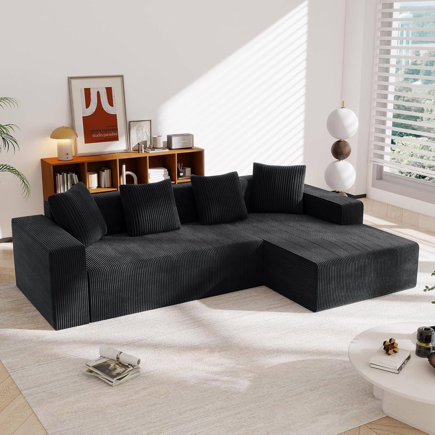 Modernes dunkelbraunes Kordsamtsektionalsofa mit fünf schwarzen Kissen in einem hellen, minimalistischen Wohnzimmer, neben einem Holzregal, einer Stehlampe und einem runden Couchtisch.