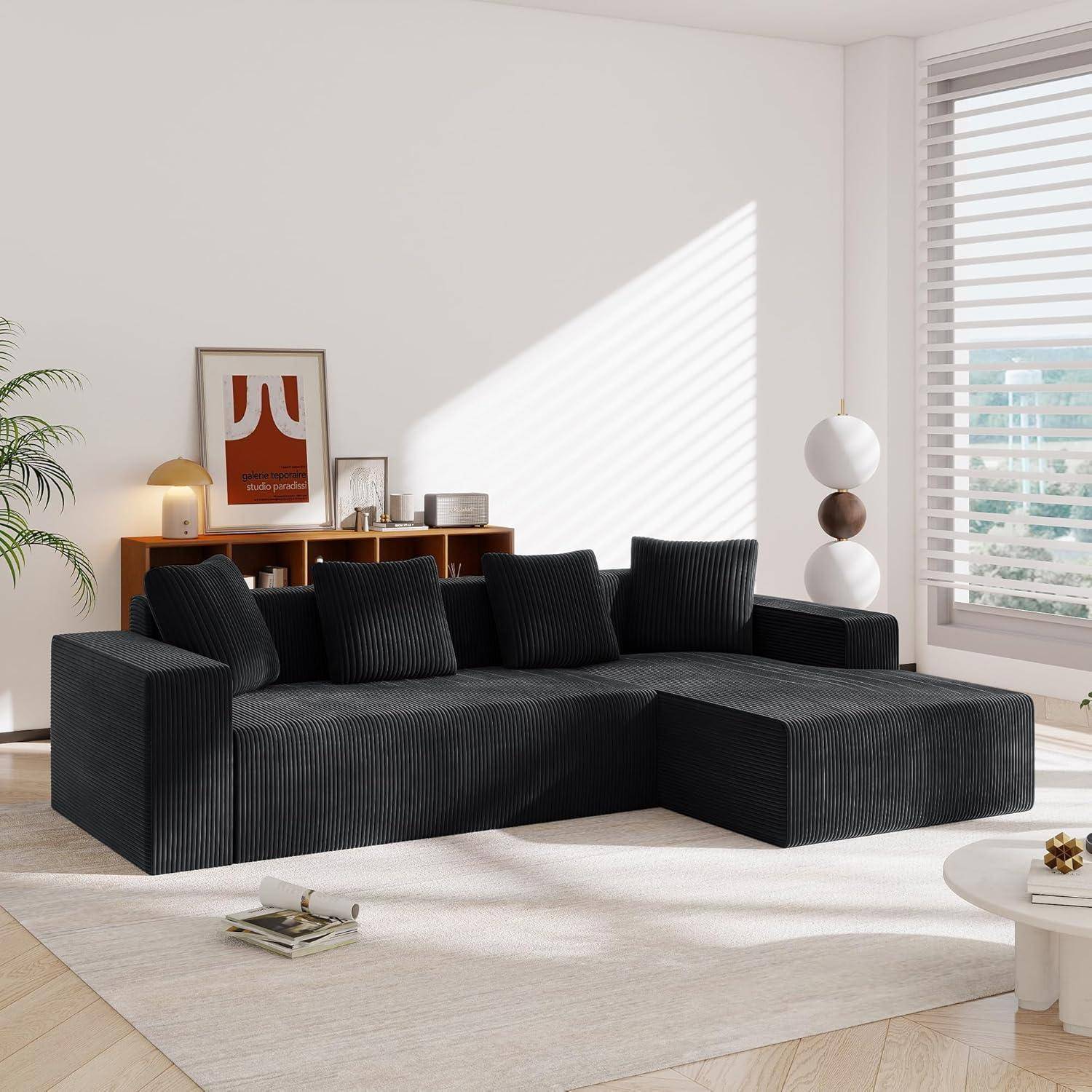 Modernes Wohnzimmer mit schwarzem Ecksofa, Kissen, hölzernem Sideboard, Stehleuchte, Wandkunst in Rahmen und hellem Sonnenlicht durch Fensterjalousien.