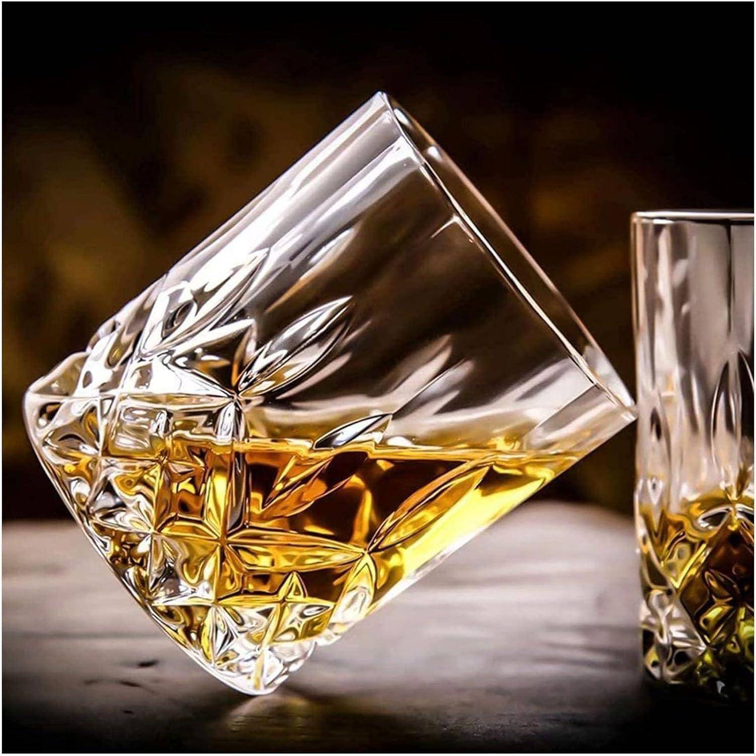 Kristallwhiskyglas auf der Seite gekippt mit bernsteinfarbener Flüssigkeit darin, neben einem aufrecht stehenden passenden Glas auf einer dunklen Oberfläche.
