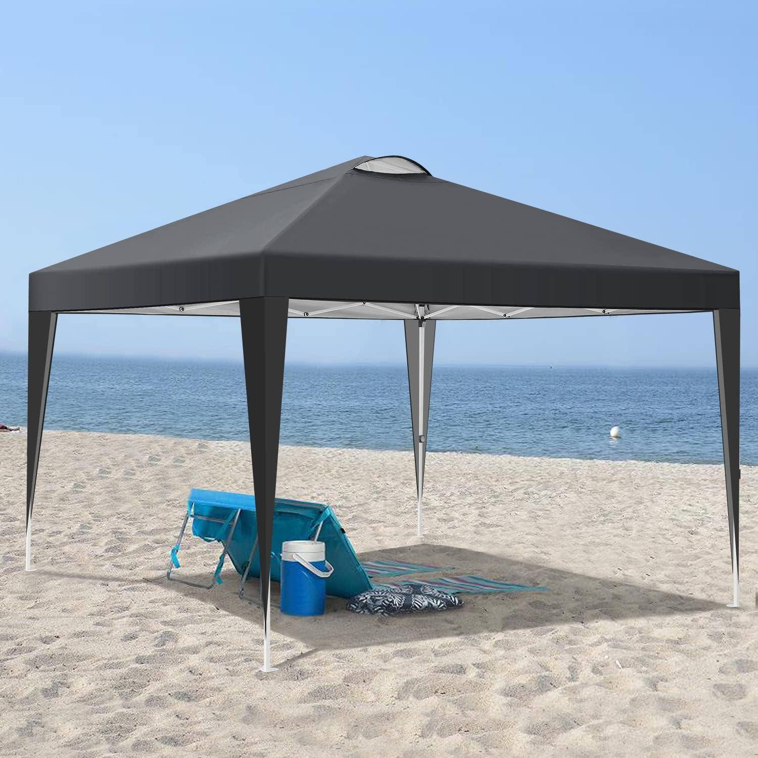 Schwarzes Strandpavillon-Zelt auf sandigem Ufer mit Kühlbox, Eimer und Matte neben ruhigem Meerwasser.