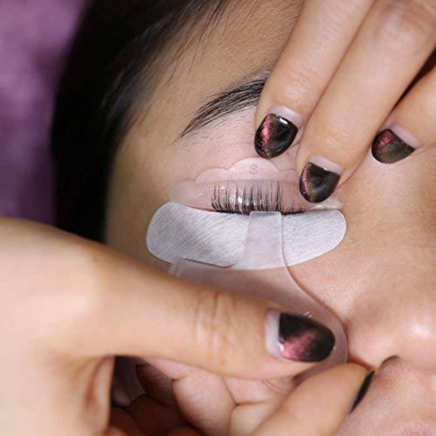 Nahaufnahme einer Person, die sich Wimpernverlängerungen anbringen lässt, wobei die Augenlider mit Klebeband offengehalten werden während der Anwendung.
