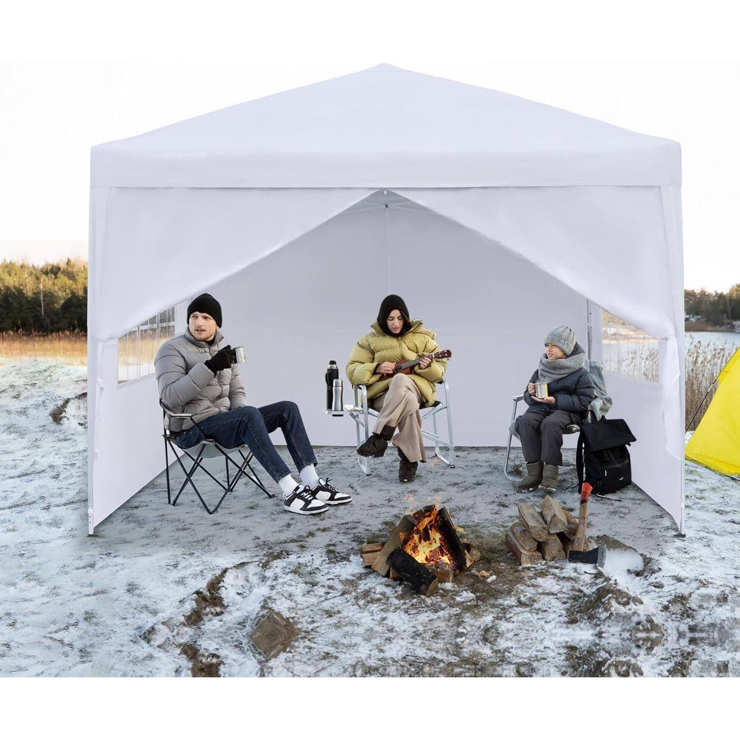 Drei Personen sitzen in einem weißen Außenpavillon-Zelt auf schneebedecktem Boden, wärmen sich an einem kleinen Feuer und tragen Winterkleidung.