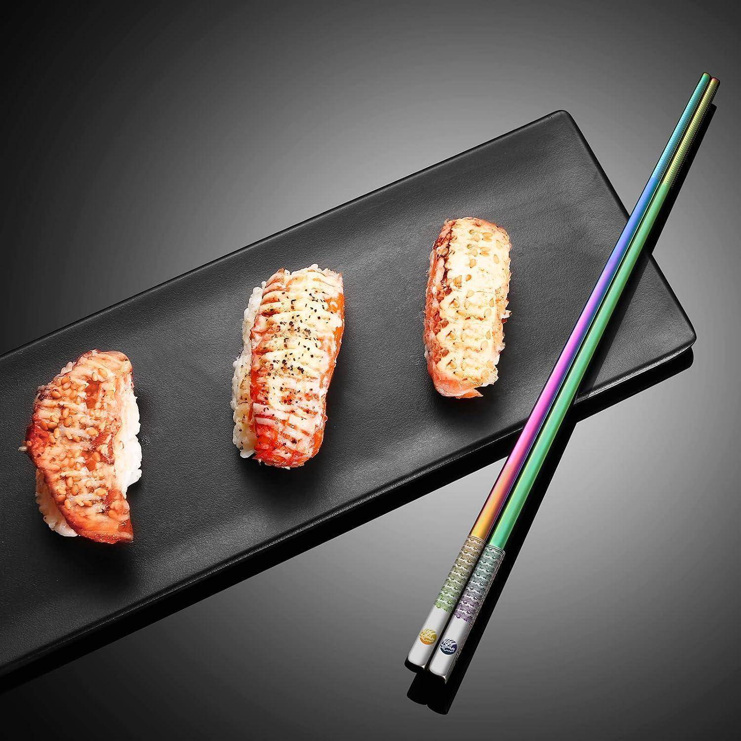 Drei Stücke Sushi auf einem schwarzen rechteckigen Teller, mit bunten Stäbchen, die diagonal daneben platziert sind.