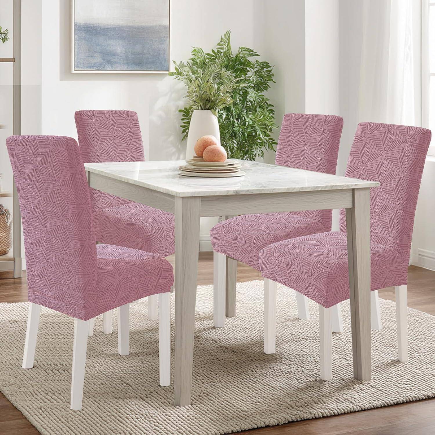 Vier rosa gemusterte Esszimmerstühle umgeben einen Tisch aus hellem Holz in einem hellen Raum mit einem Teppich und einer Pflanzendeko in der Mitte.