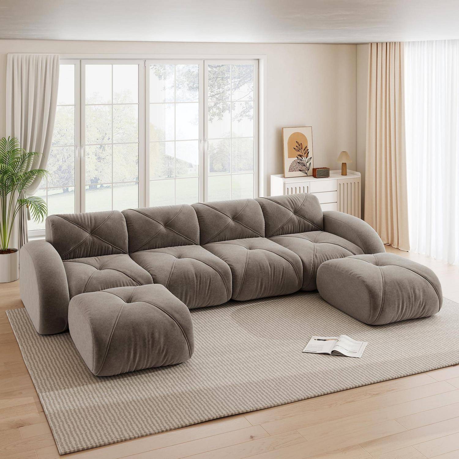 Weiche modulare graue Polster-Eckgarnitur mit übergroßen Kissen in einem hellen minimalistischen Wohnzimmer, auf einem beigen Teppich neben großen Fenstern und Vorhängen.