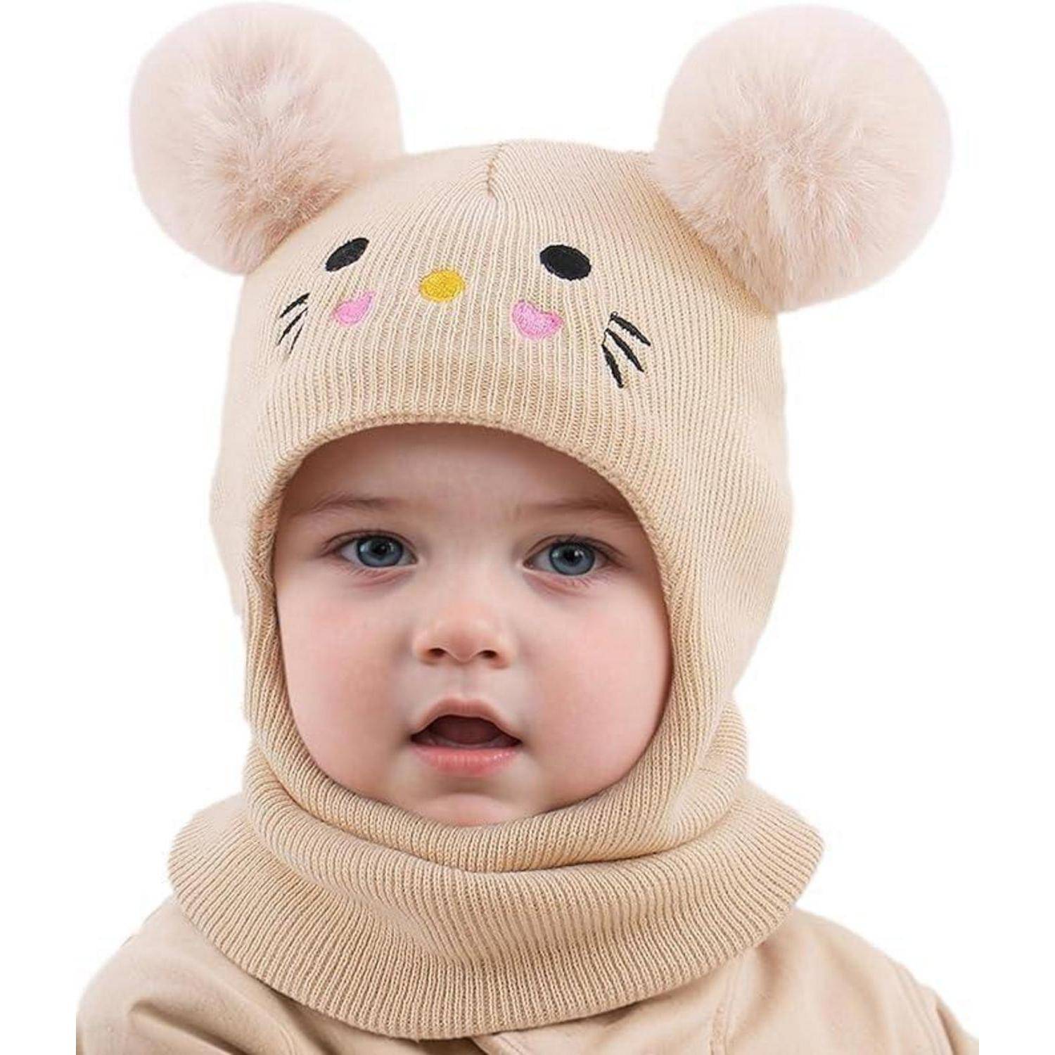 Baby mit einer beigen Strickmütze mit Bommel-Ohren und einem passenden Nackenwärmer, mit einem süßen Tiergesicht auf der Kapuze.