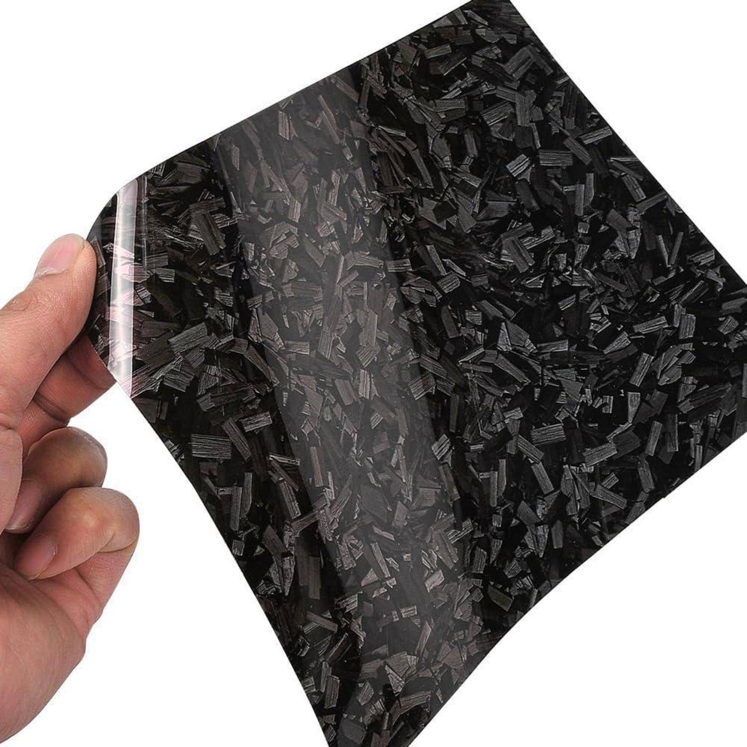 Hand hält ein flexibles schwarzes gemustertes Blatt mit glänzender Oberfläche gegen einen weißen Hintergrund.