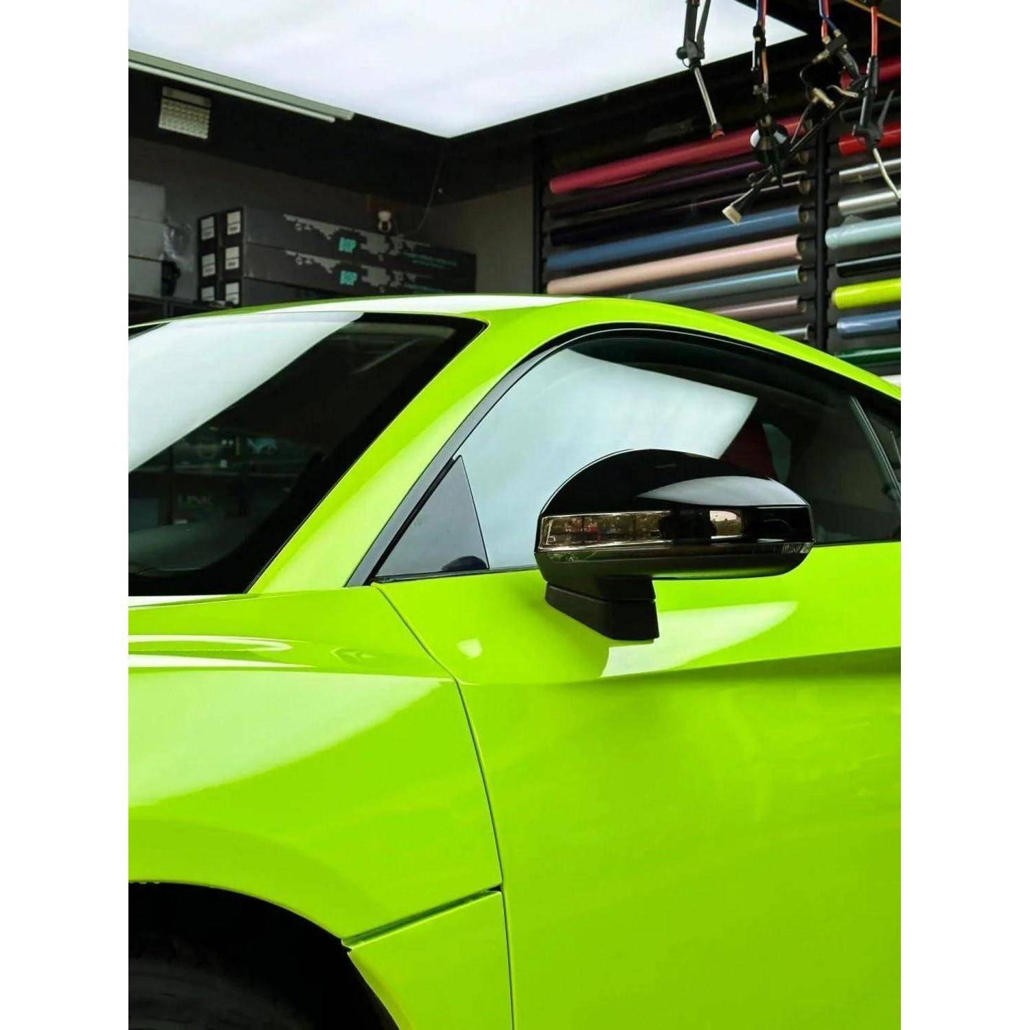 Nahaufnahme eines hellgrünen Sportwagens in einer Detailingwerkstatt, die das Seitenfenster und den Spiegel mit gerollten Vinylfolien im Hintergrund zeigt.