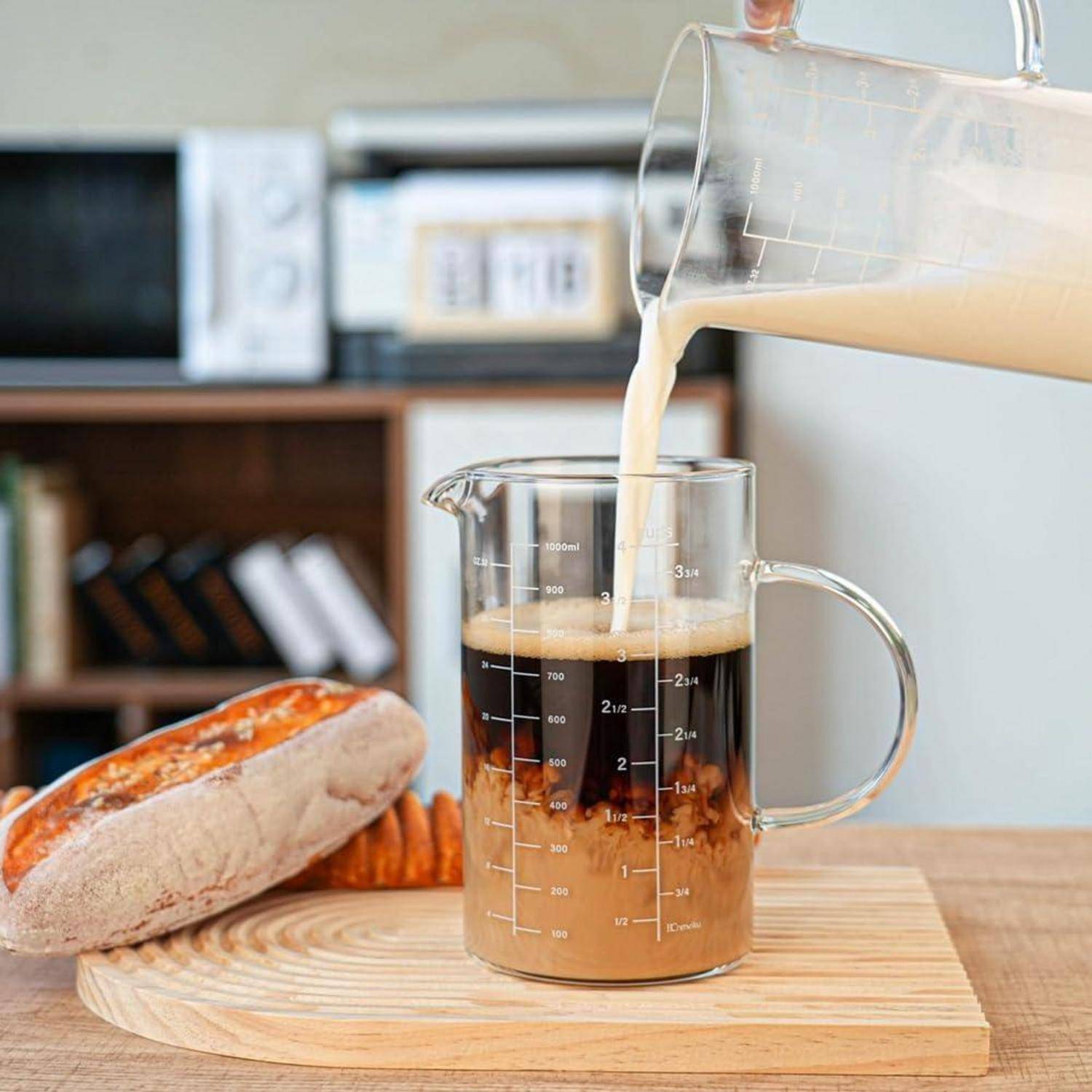 Milch wird in einen Glaskaffeemessbecher auf einem Holzbrett gegossen, mit einem Laib Brot und Keksen daneben.