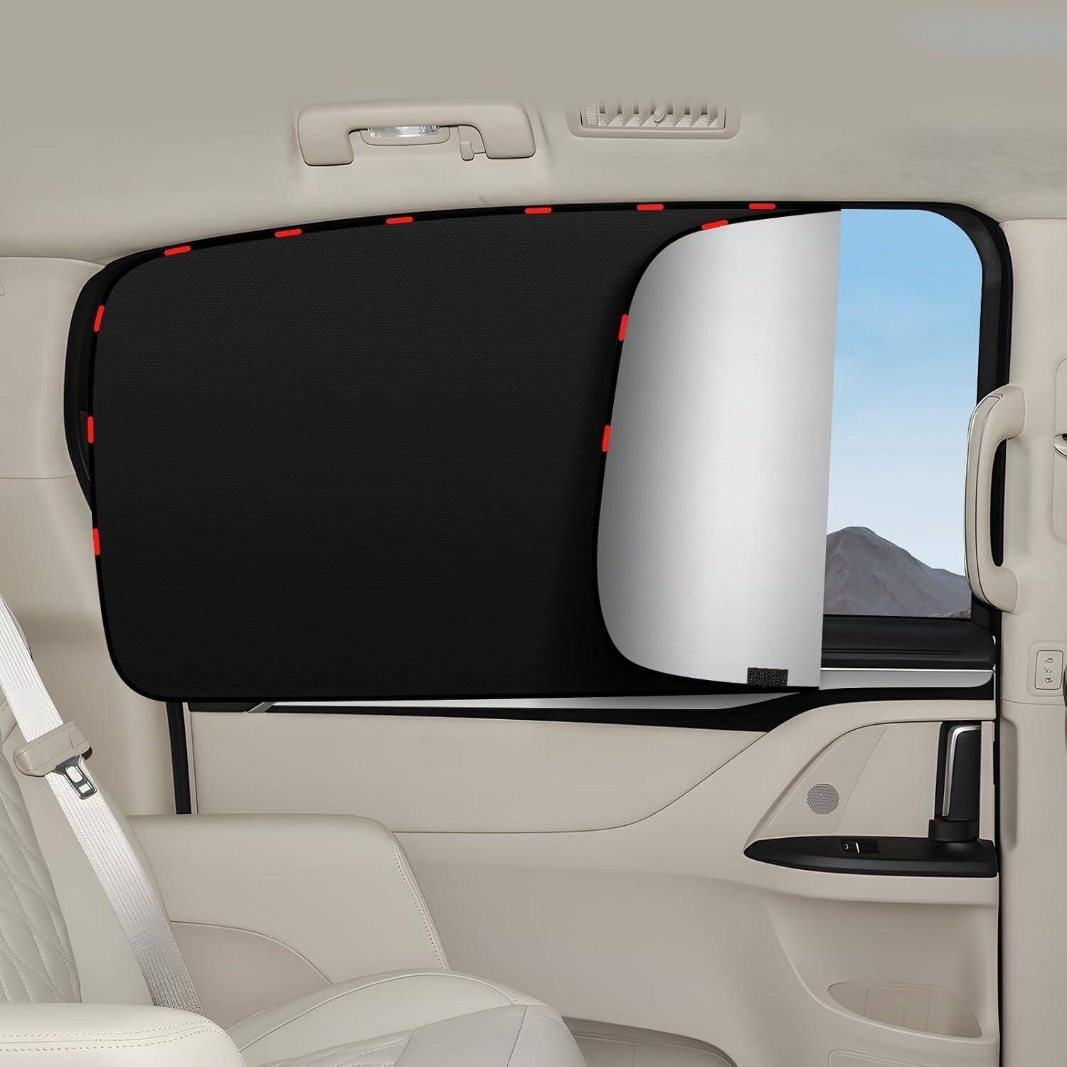Hinteres Seitenfenster eines Autos mit einem schwarzen Sonnenschutz und einer teilweise heruntergelassenen weißen Jalousie, die einen schmalen Blick auf Himmel und Berge freilässt.