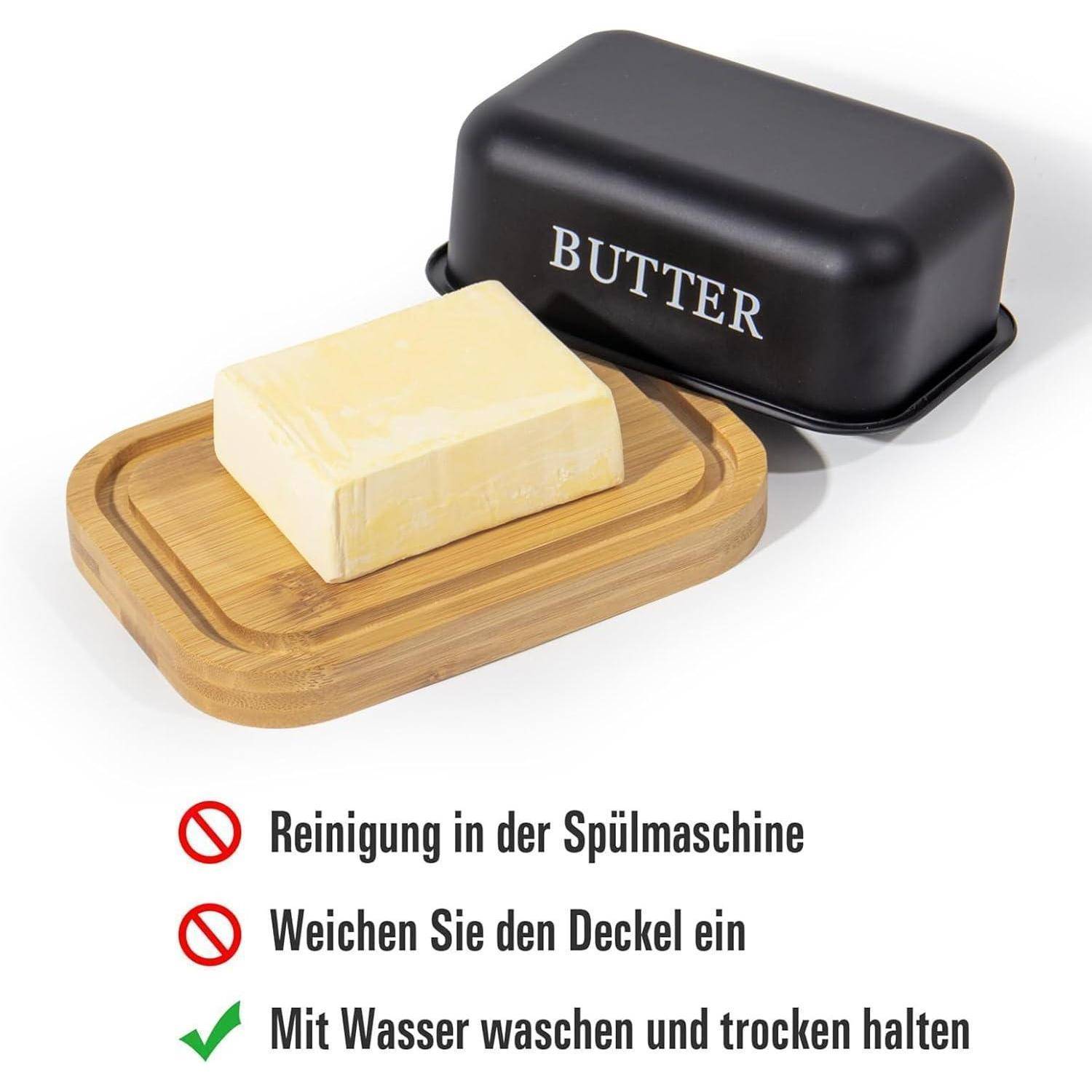 Butter auf einem Holztablett neben einer schwarzen Butterdose mit der Aufschrift „BUTTER"; darunter besagen deutsche Pflegeanweisungen, die Spülmaschine nicht zu verwenden, den Deckel einzuweichen und von Hand zu waschen und zu trocknen.