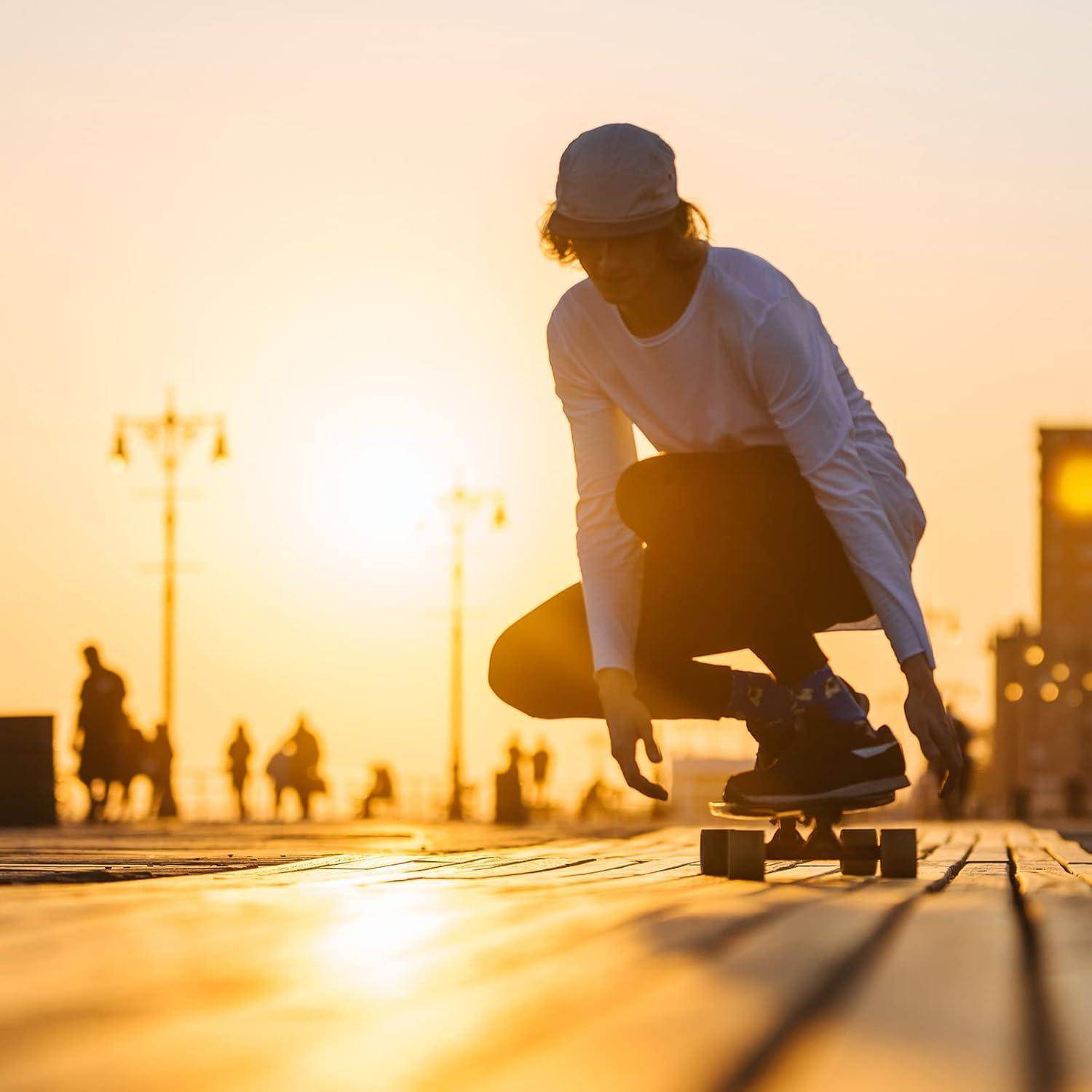 Person kauert auf einem Skateboard auf einem Gehweg bei Sonnenuntergang, mit silhouettierten Fußgängern und Straßenlaternen im Hintergrund.