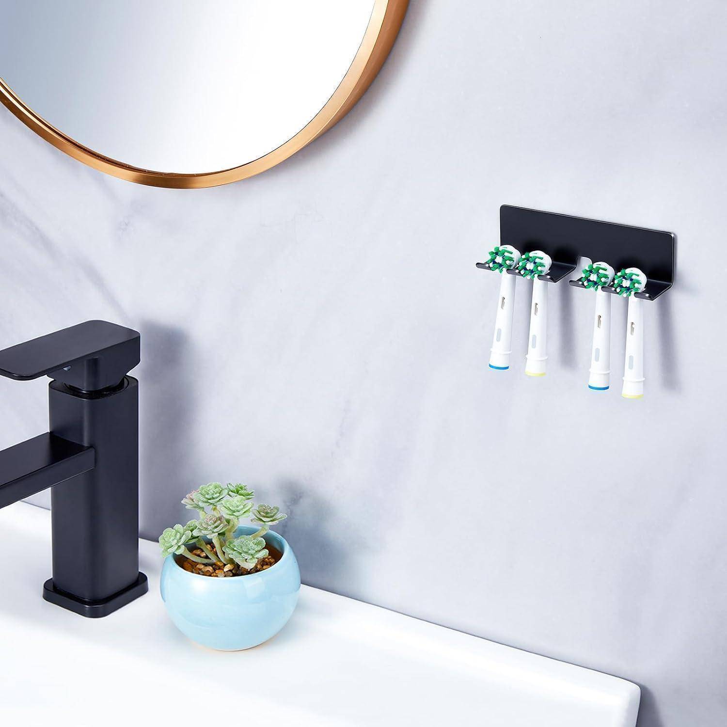 An der Wand montierter Zahnbürstenhalter mit vier elektrischen Zahnbürsten neben einem schwarzen Wasserhahn, Spiegelkante und einer kleinen Topfpflanze mit Sukkulente auf einer Badezimmerablage.