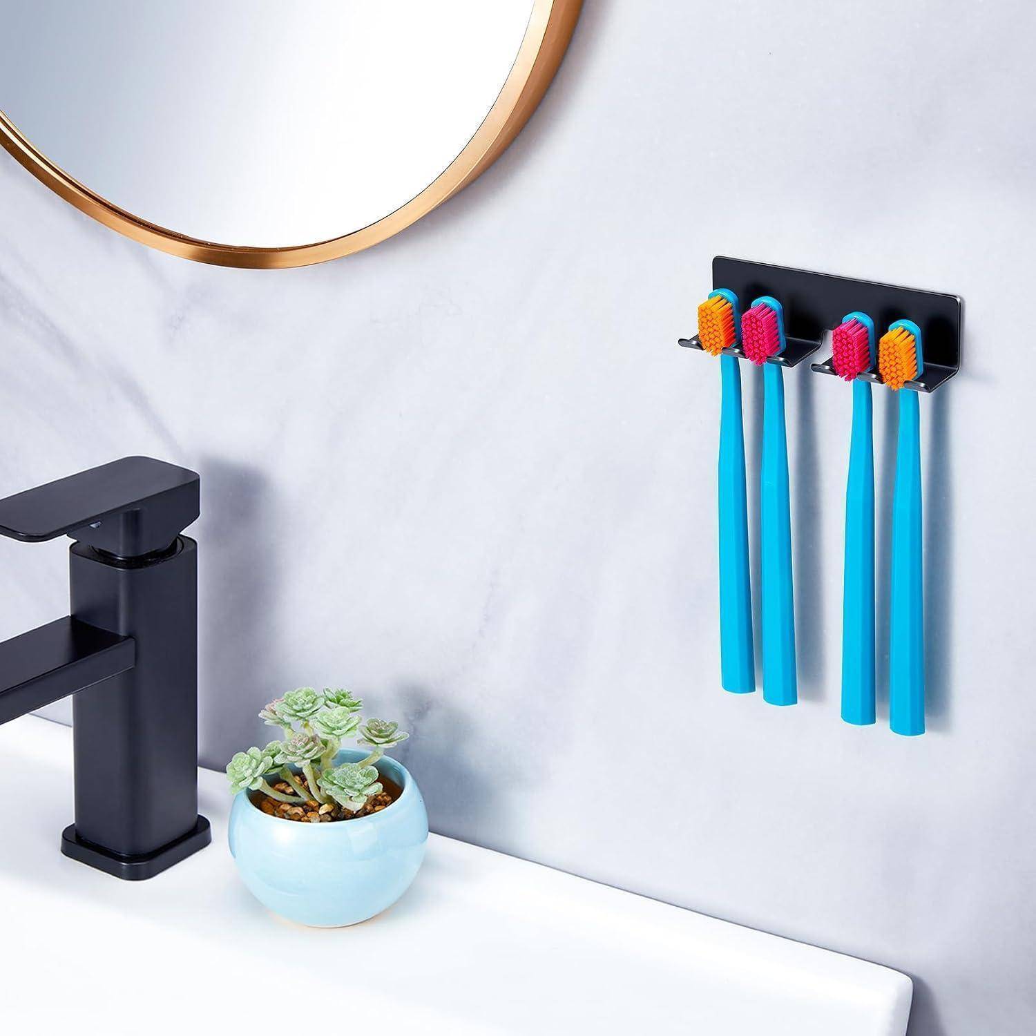 Badezimmerwaschbeckenbereich mit an der Wand montiertem Zahnbürstenhalter und vier blauen Zahnbürsten neben einem schwarzen Wasserhahn, kleiner Topfpflanze und Rand eines runden Spiegels.