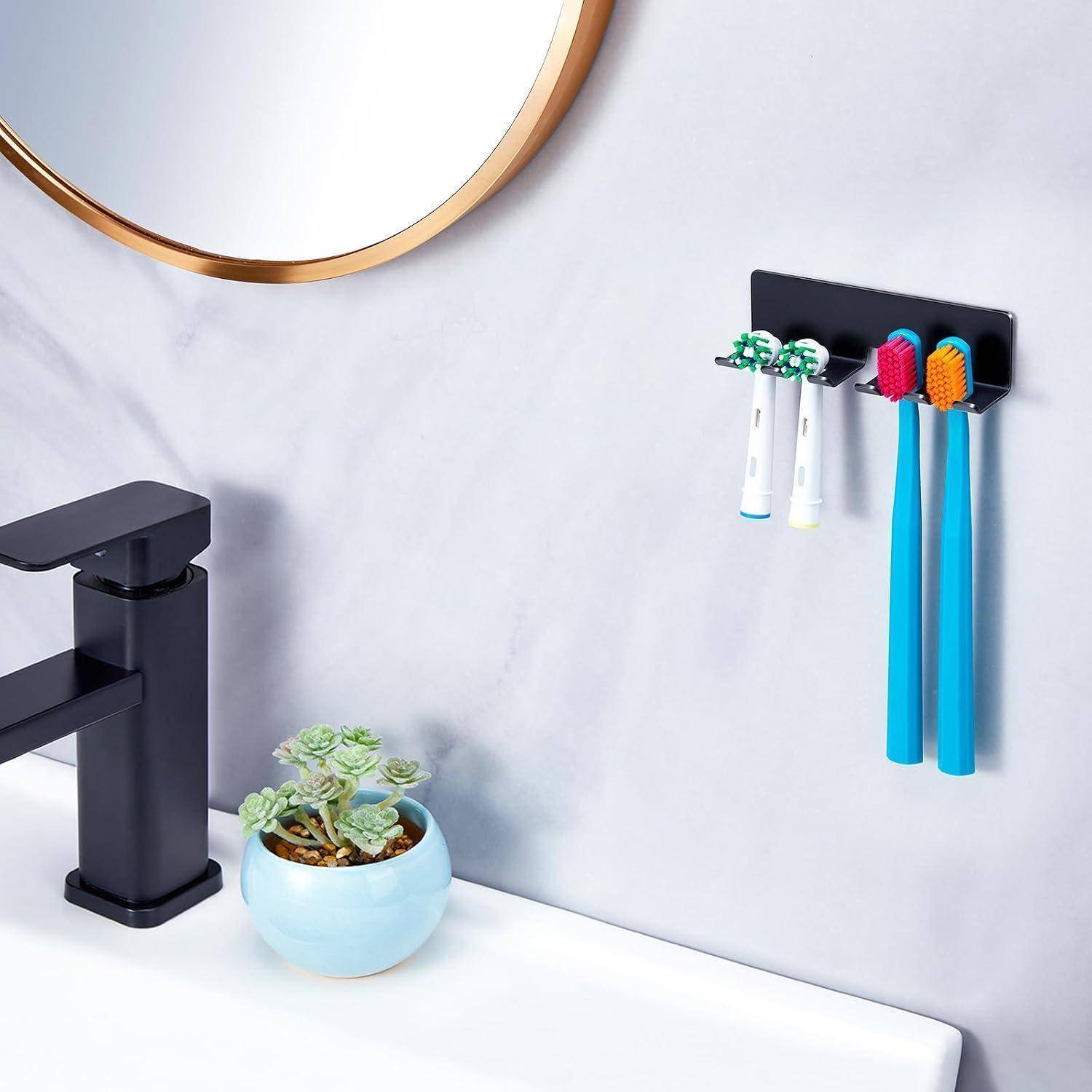 Badezimmerwaschbereich mit schwarzem Wasserhahn, rundem Spiegel, kleinem Sukkulenten und an der Wand montiertem Halter, in dem zwei Zahnbürsten und zwei Zahnpastatuben aufbewahrt werden.