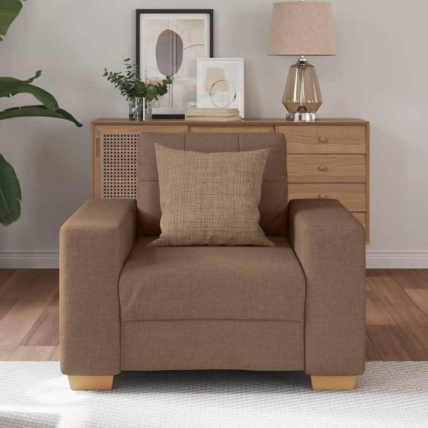 Brauner Sessel mit beigem Kissen in einem modernen Wohnzimmer, positioniert vor einem hölzernen Sideboard mit Lampe und Bilderrahmen.