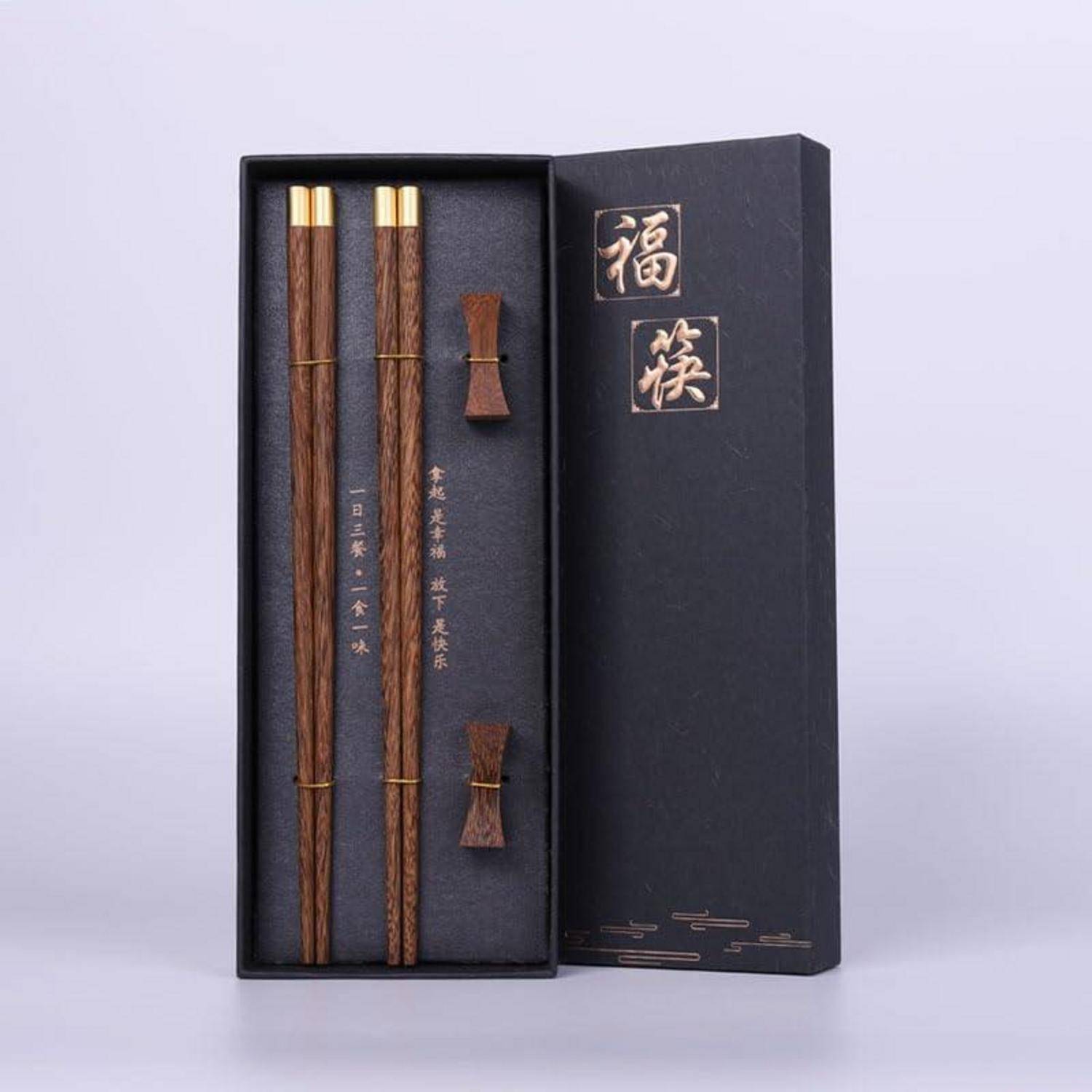 Offene schwarze Geschenkbox mit Paar Holzstäbchen mit Goldspitzen und kleine passende Unterlagen, beschriftet mit chinesischen Zeichen auf dem Deckel.