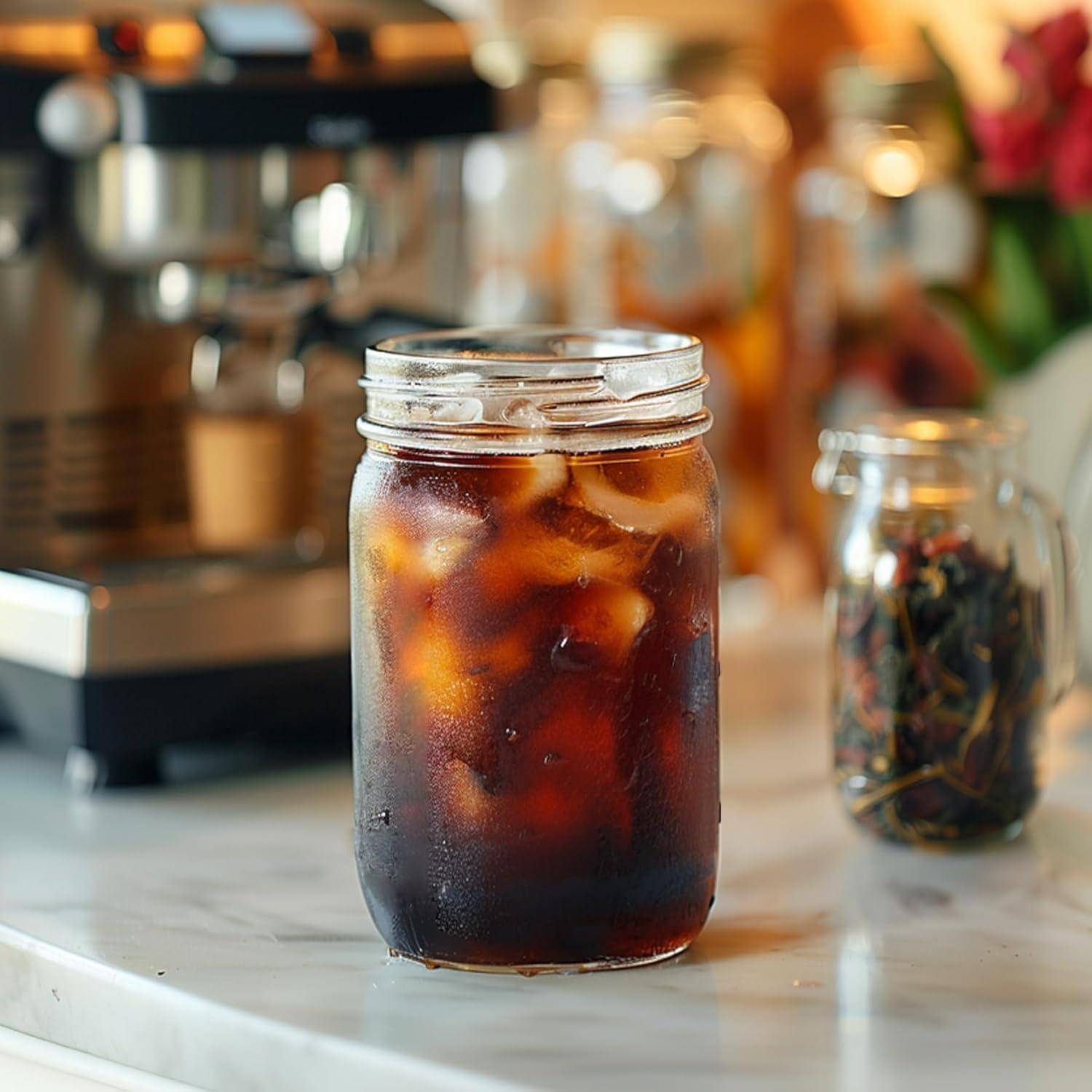 Ein Einmachglas gefüllt mit Eiskaffee steht auf einer Arbeitsplatte, mit einer unscharfen Kaffeeausstattung im Hintergrund.