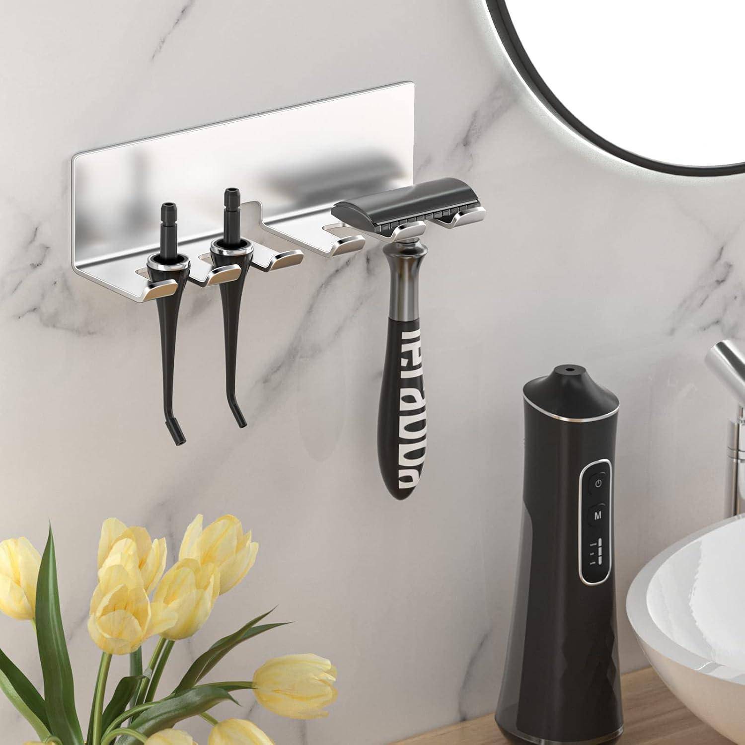 An der Wand montierter Badezimmerorganizer mit zwei Zahnbürsten und einem Rasierer über einem Waschbecken, mit einer elektrischen Zahnbürste, einer Schüssel und Blumen auf der Arbeitsplatte.