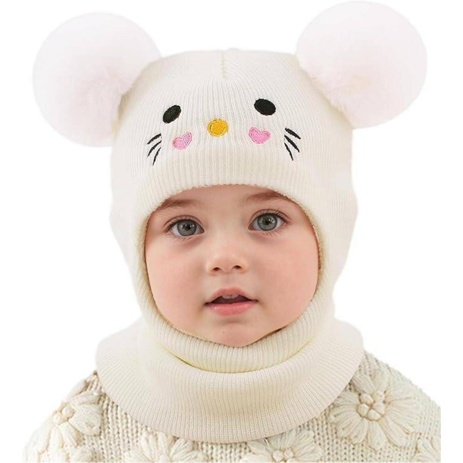 Porträt eines Babys, das eine weiße Strickmütze mit Mausohren und einen passenden Schal trägt, frontal gegen einen neutralen Hintergrund ausgerichtet.