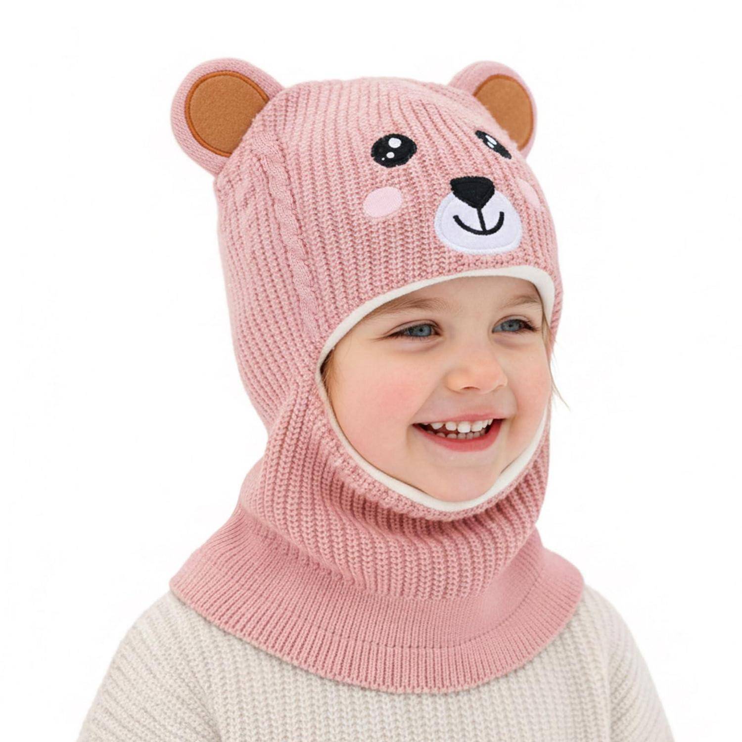 Lachendes Kind, das eine rosa gestrickte Bärenmütze und einen cremefarbenen Pullover vor einem einfachen weißen Hintergrund trägt.